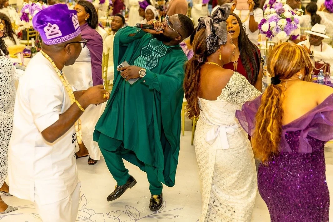 People dancing and socializing at a wedding reception with purple and white floral decorations.