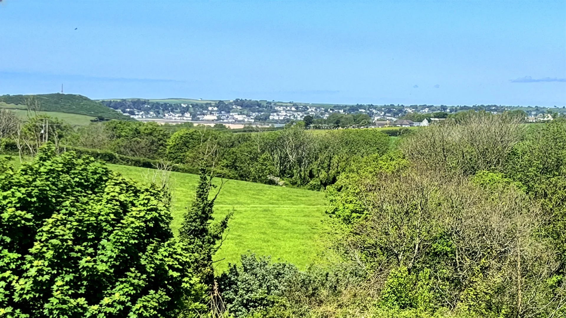 A scenic view of green fields and trees with a distant town and blue sky in the background.