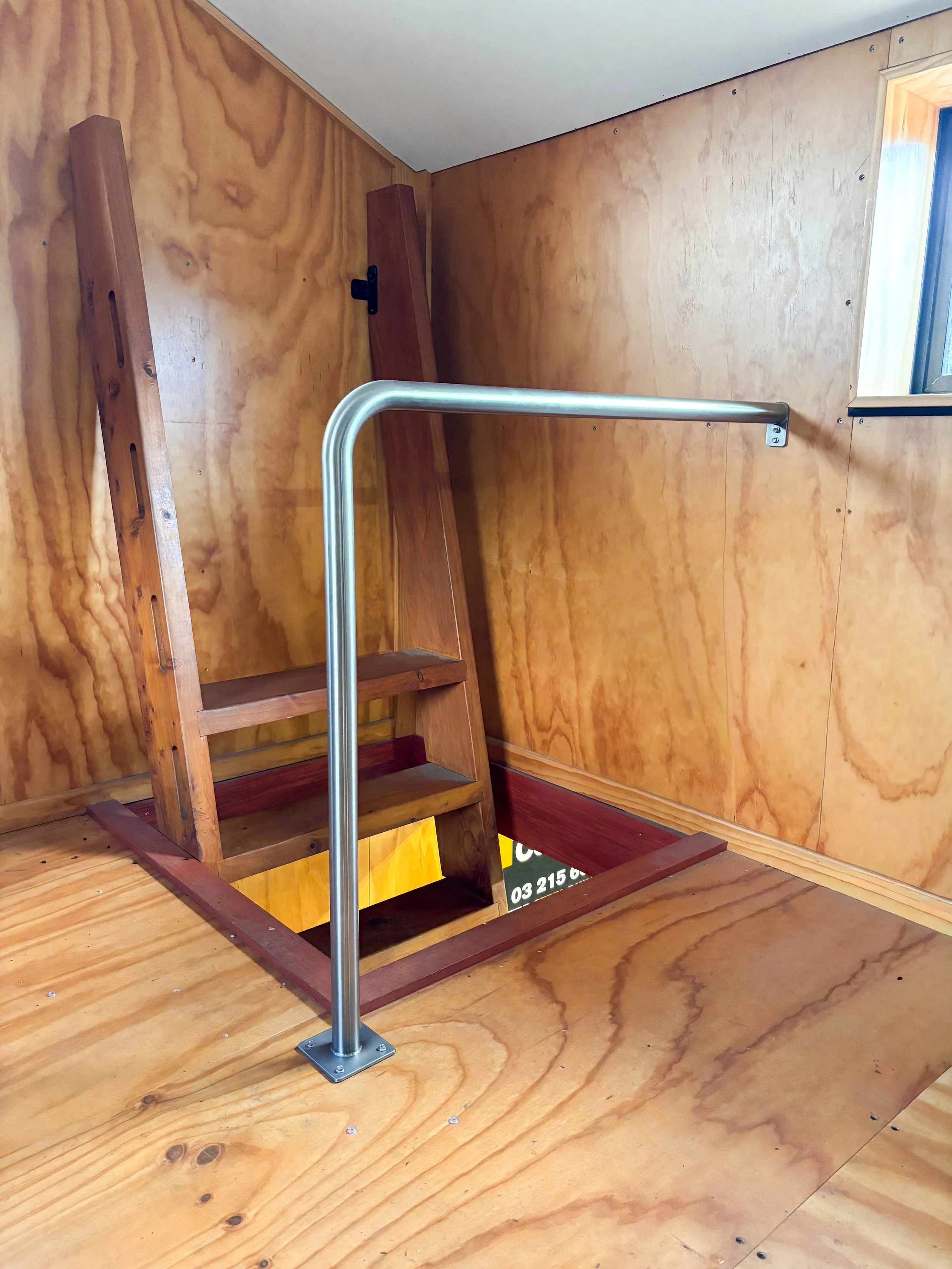 Photo of an unfinished wood staircase with metal railing, surrounded by wood-paneled walls and floor.
