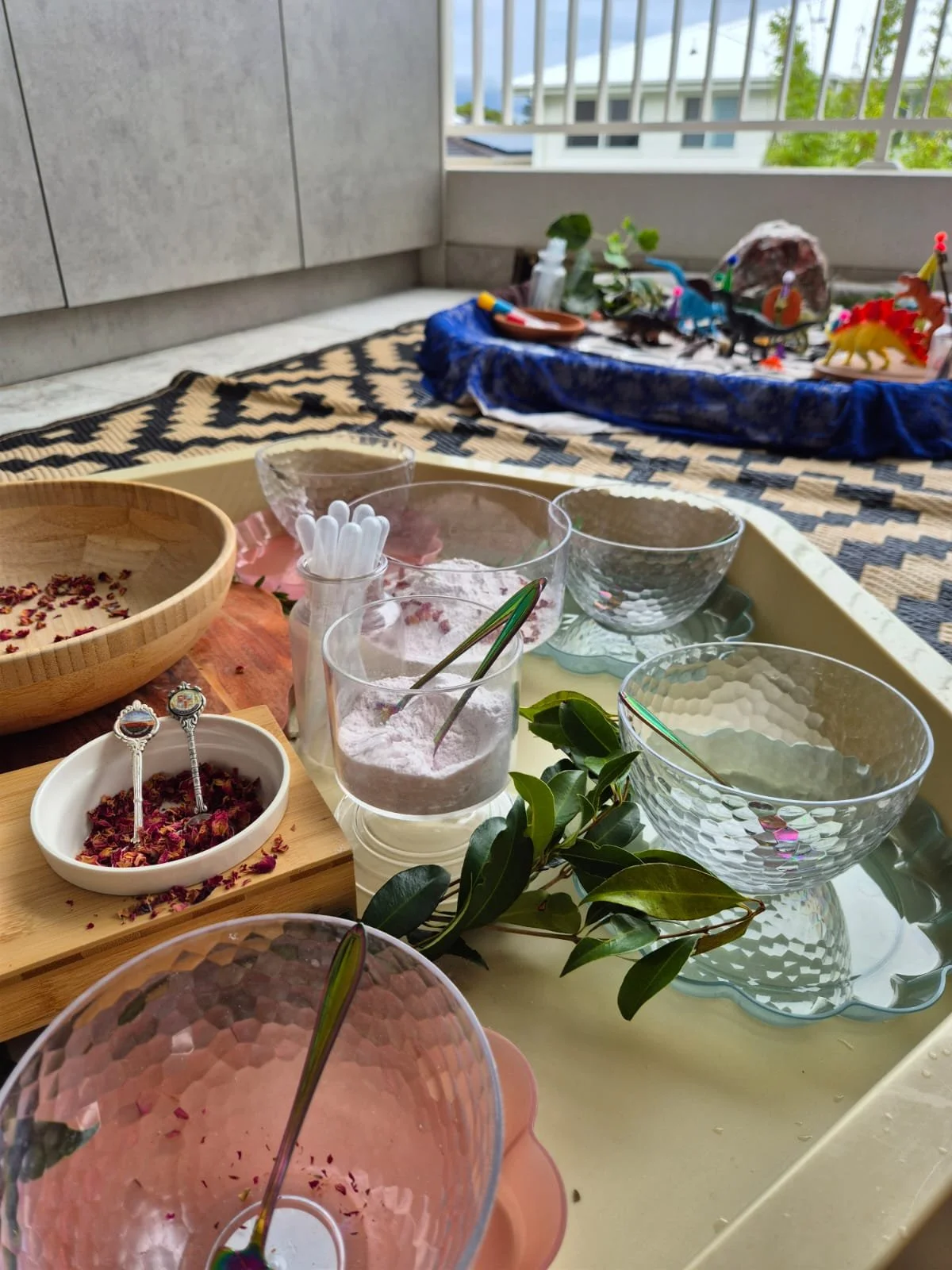 A table with bowls, glasses, and utensils, featuring dried flowers and green leaves, set on a yellow tray.