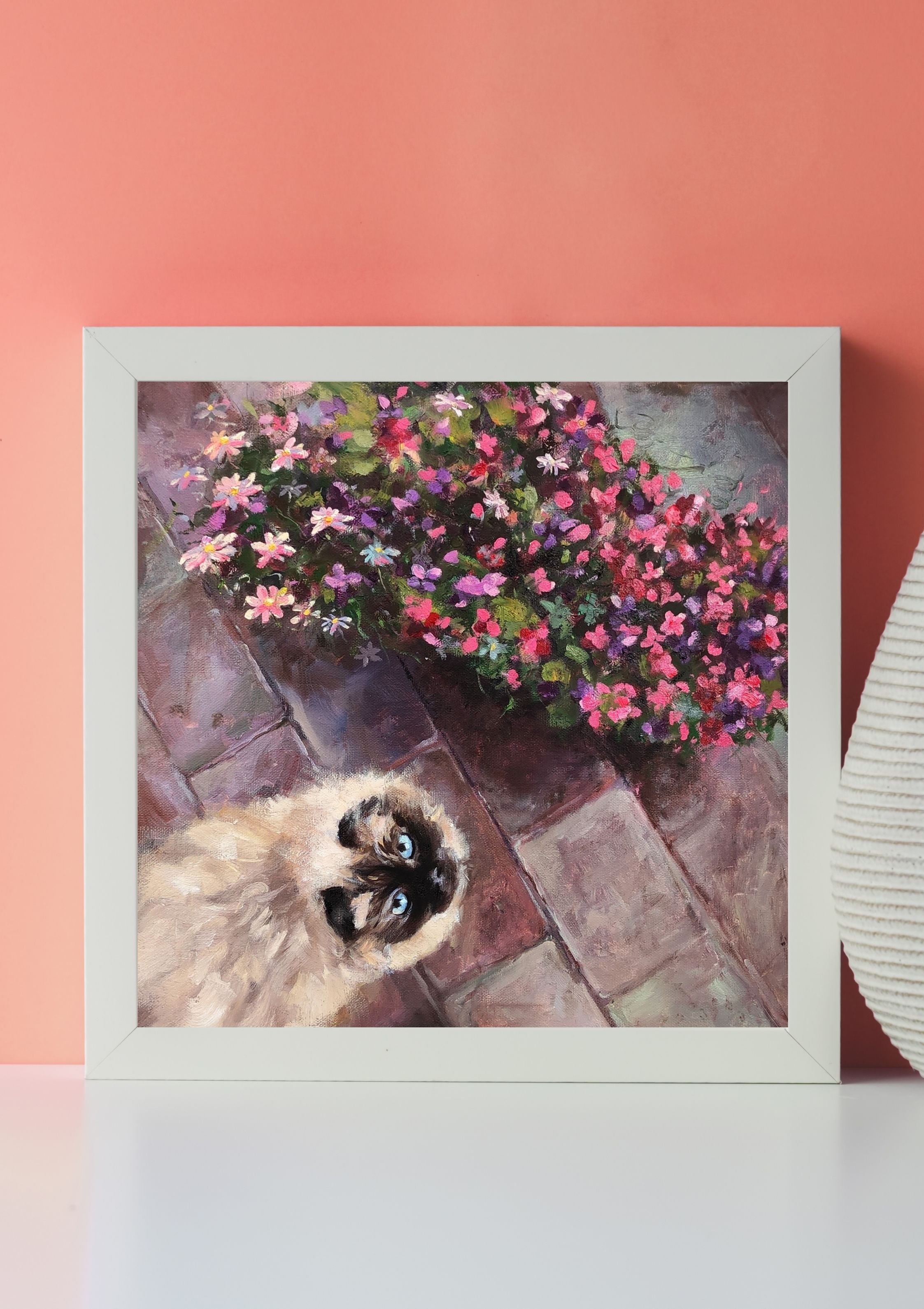 Painting of a Siamese kitten looking up, surrounded by pink, purple, and white flowers, set against a background of a brick patio and a pink wall.