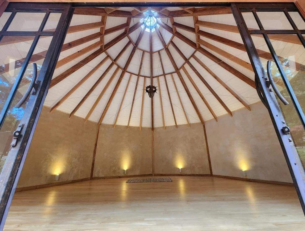 View of a round, wooden gazebo with a peaked roof and open glass doors.