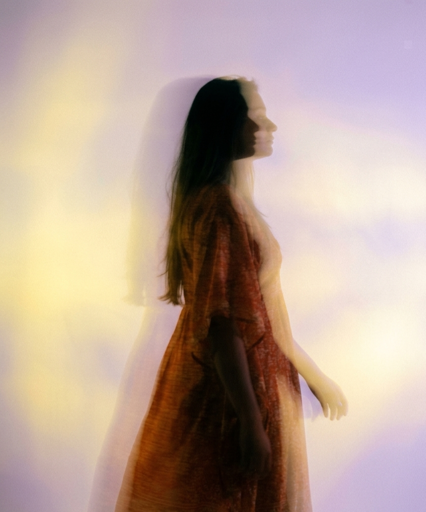 Blurred silhouette of a woman in a dress standing sideways against a colorful, abstract background.