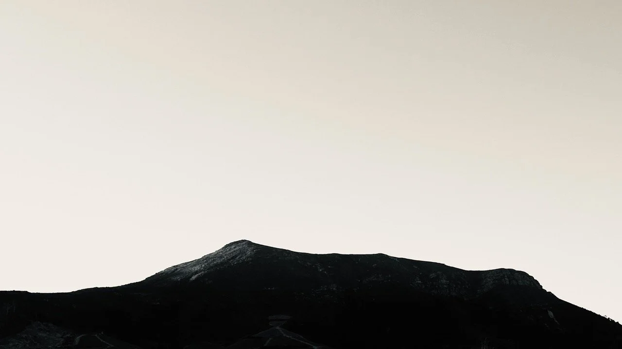 Silhouette of a mountain range against a pale, cloudy sky - Ken Kamara