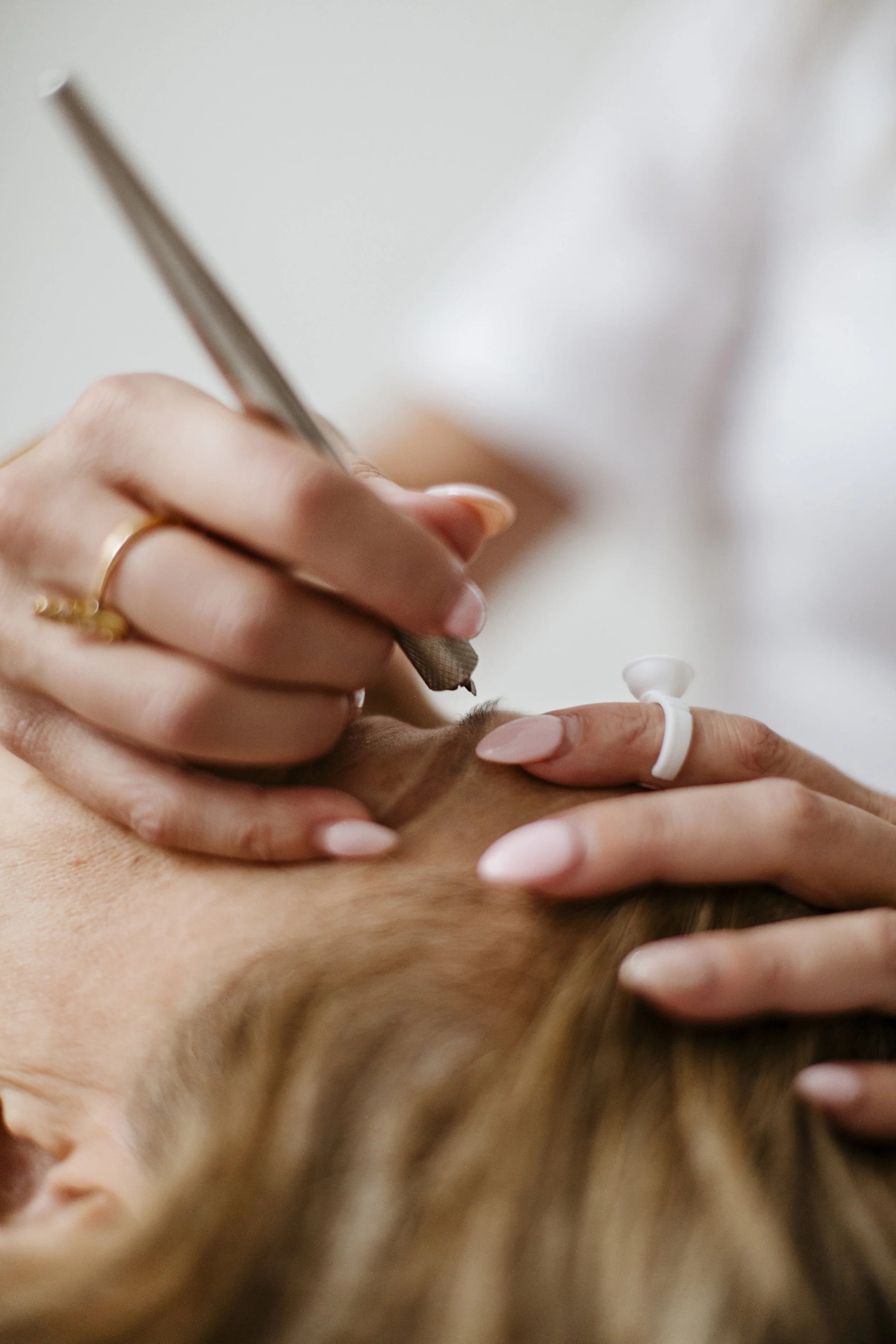 Close-up of cosmetic tattooing being performed on eyebrows, using a precision tool to create soft, natural brow strokes.