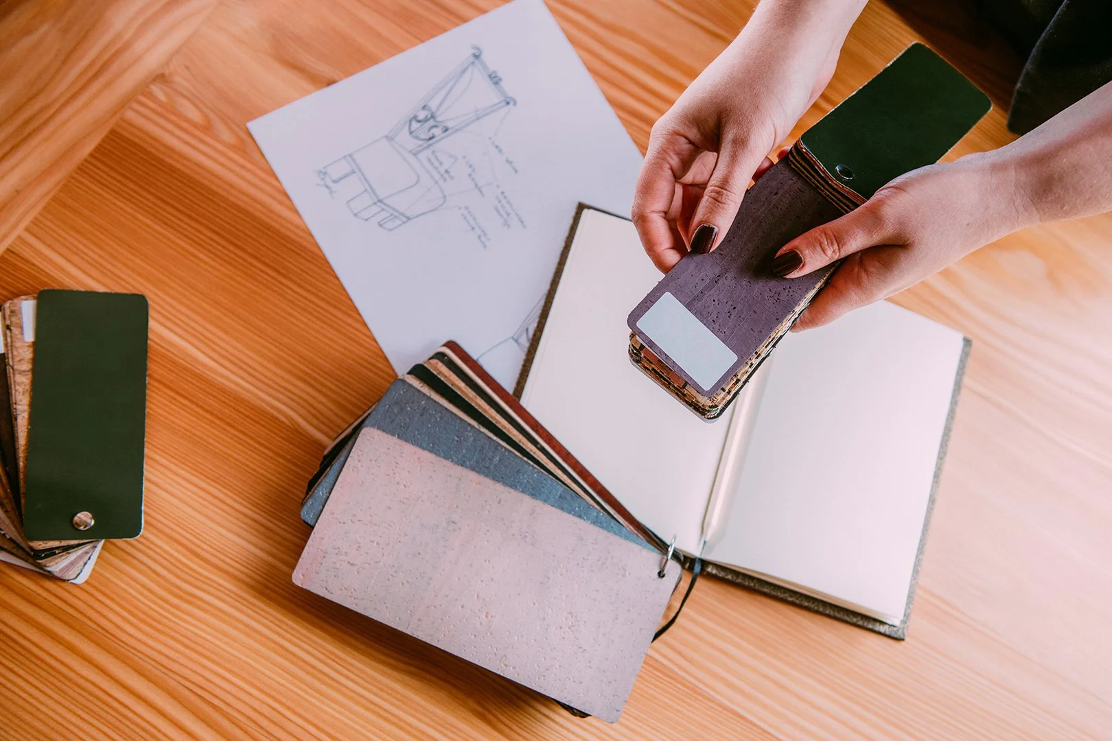 A person holding color samples or paint swatches over a table with more swatches, a notebook, and a sketch of a chair.