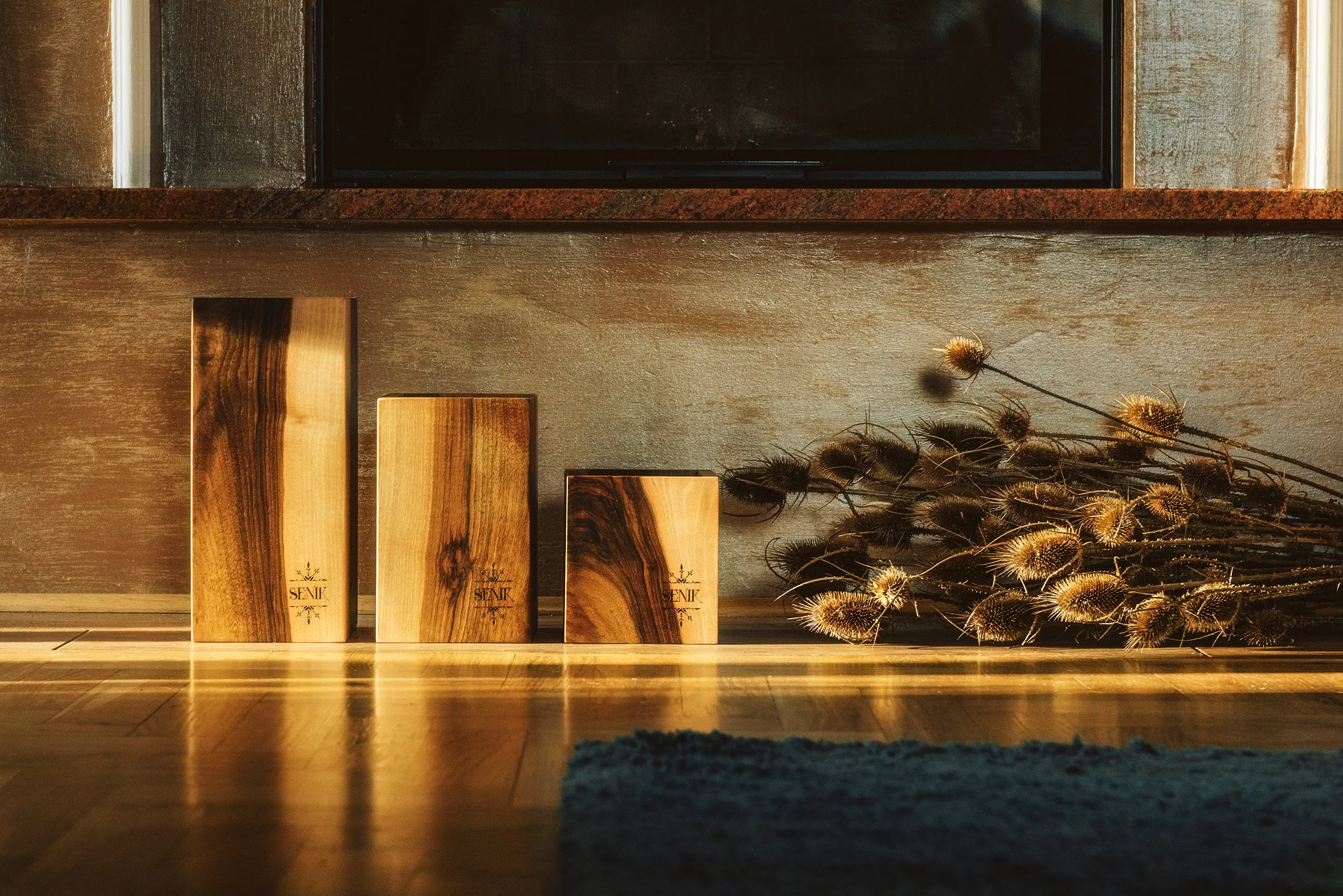 Photo of a fireplace mantel with wooden plaques and dried thistle flowers, illuminated by warm lighting, with a black framed TV mounted above.