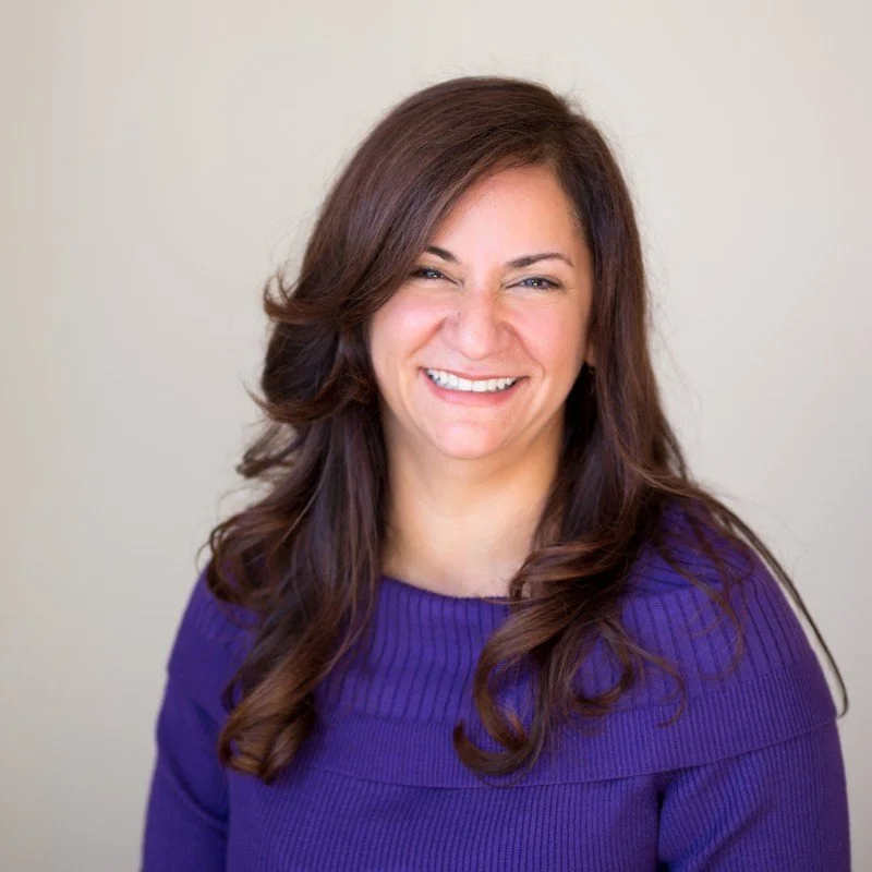 Kathy Jeffery with dark brown hair wearing a purple sweater smiling against a light background.