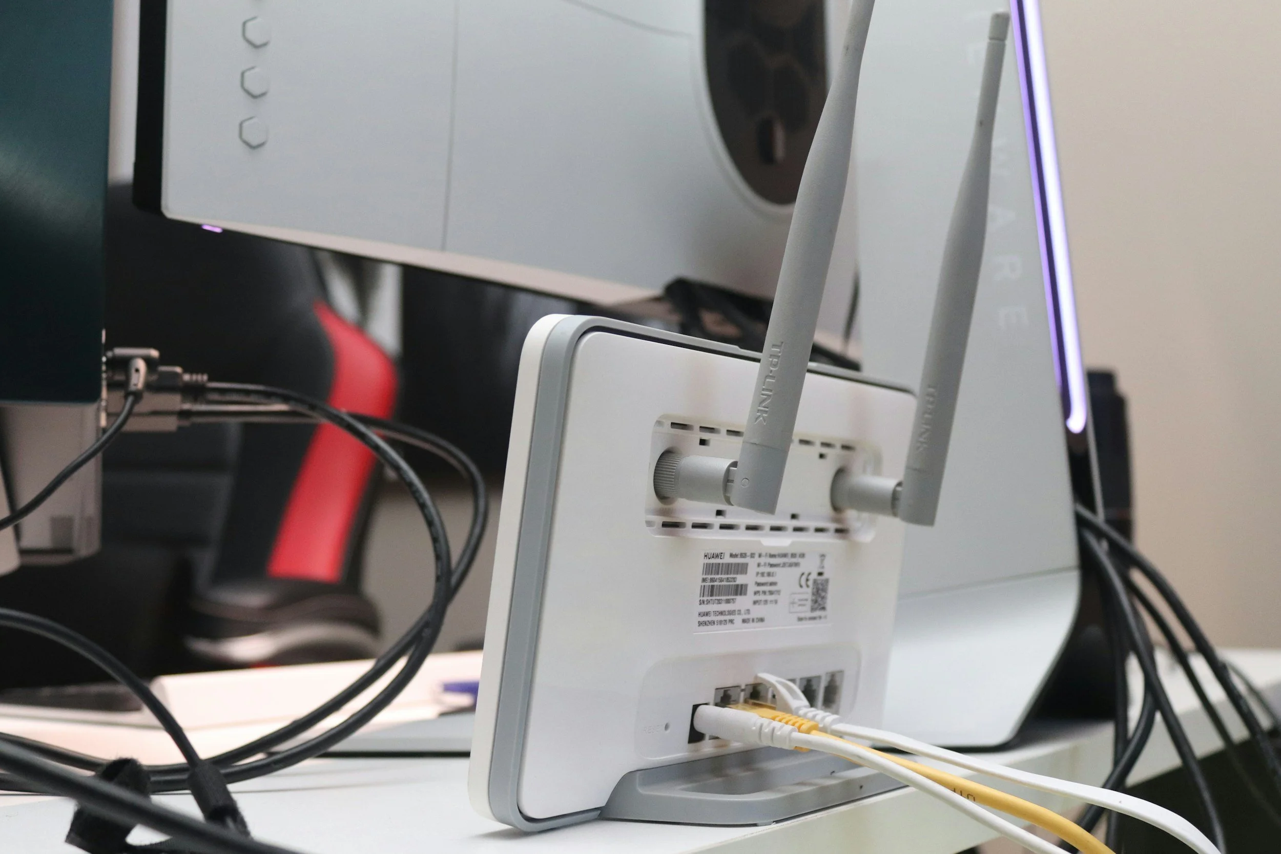 Close-up of a white Wi-Fi router with multiple cables connected at the back, in an office or tech environment.