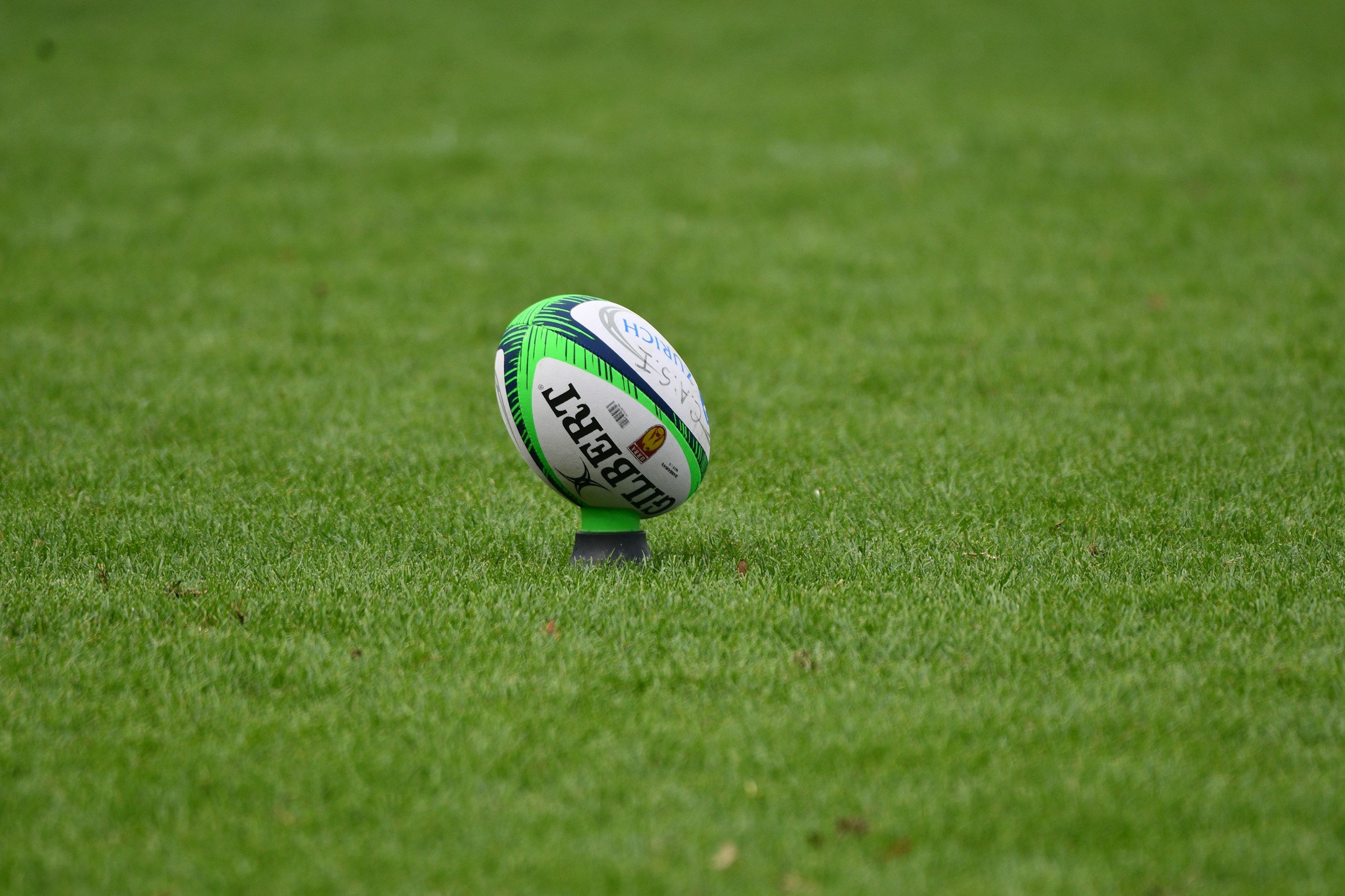 A rugby ball resting on a tee on a grassy field.
