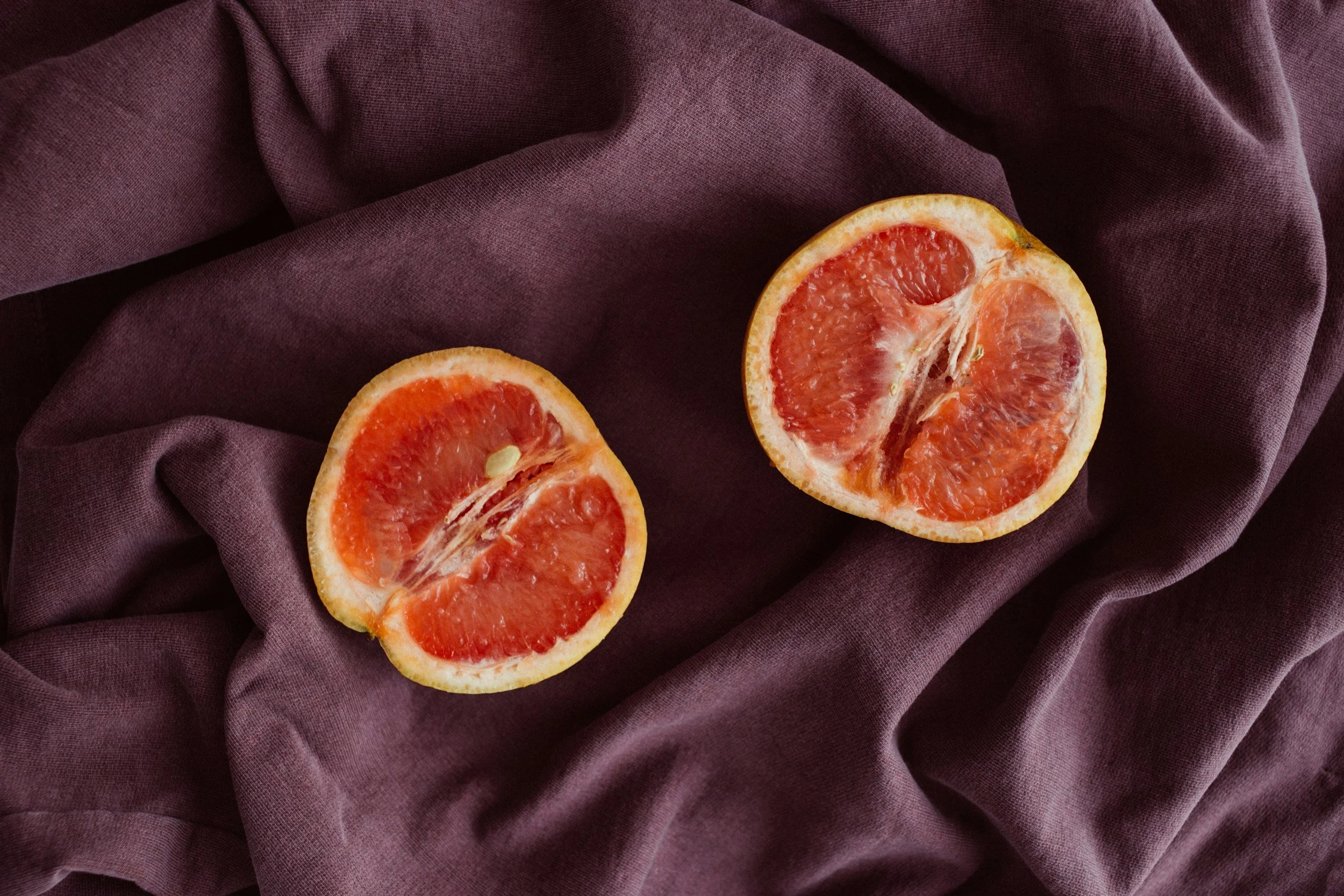 a grapefruit split in half positioned suggestively on purple bed sheets