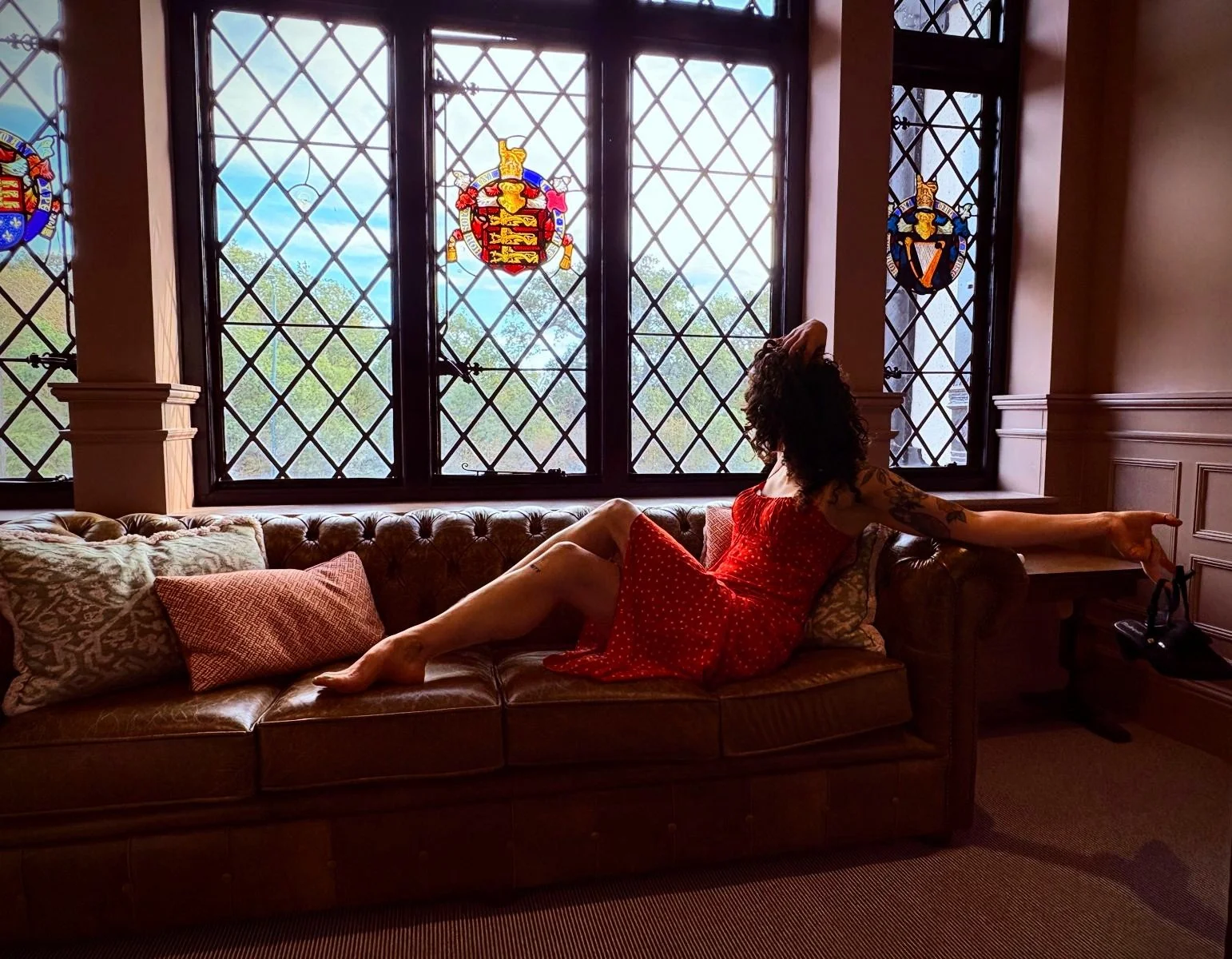 Celine, independent London companion  reclines on a luxurious sofa in a high end hotel in London. She wears a silk dress, and her legs and feet are bare, showing off her gorgrously curvy natural figure.