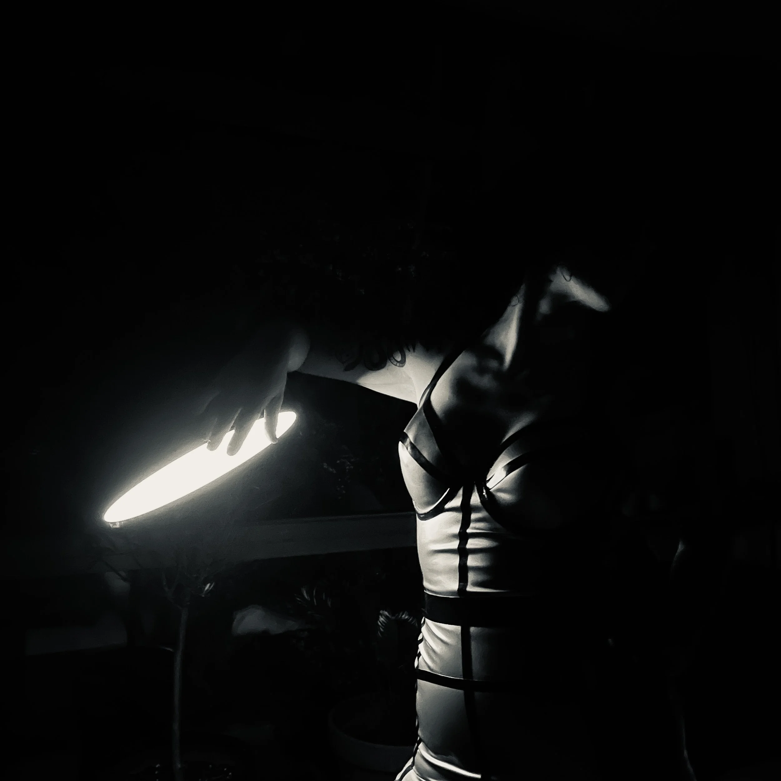 Dark scene with a narrow, bright line of light running diagonally across the image, with some indistinct objects and shapes surrounding it.