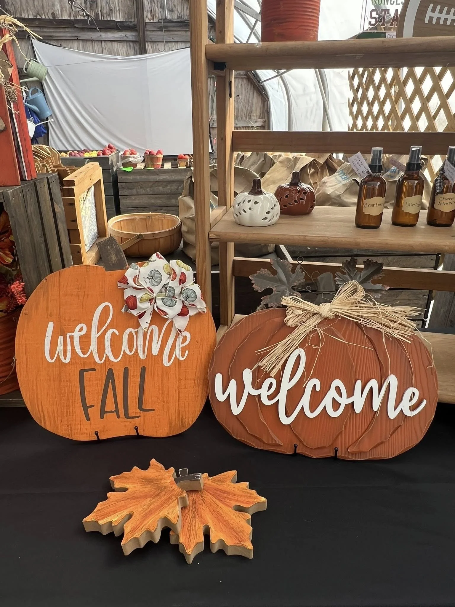 Decorative fall-themed signs and decorations, including orange pumpkins with white and brown accents, and a wooden or metal maple leaf shape, displayed on a table or shelf.