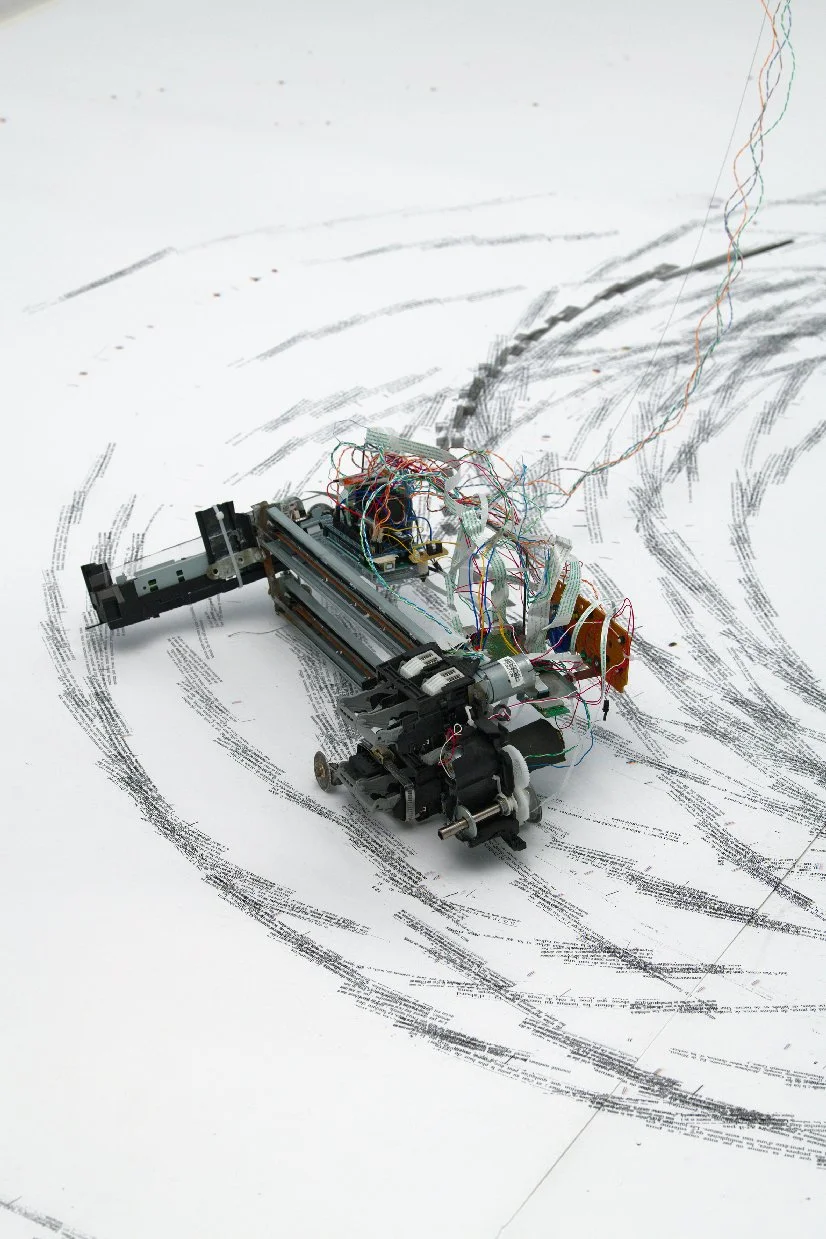 Un robot en construction avec des fils électriques, placé sur un plan avec des schémas ou dessins techniques autour.