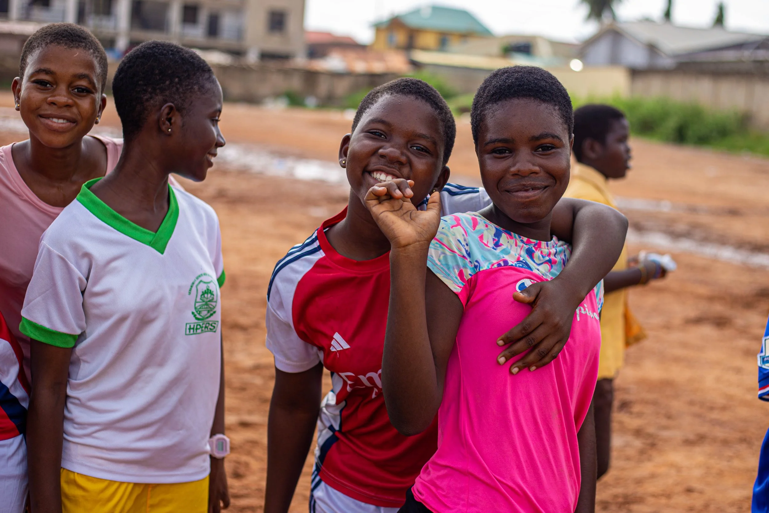 A group of children smiling and playing outdoors in a neighborhood with houses in the background.