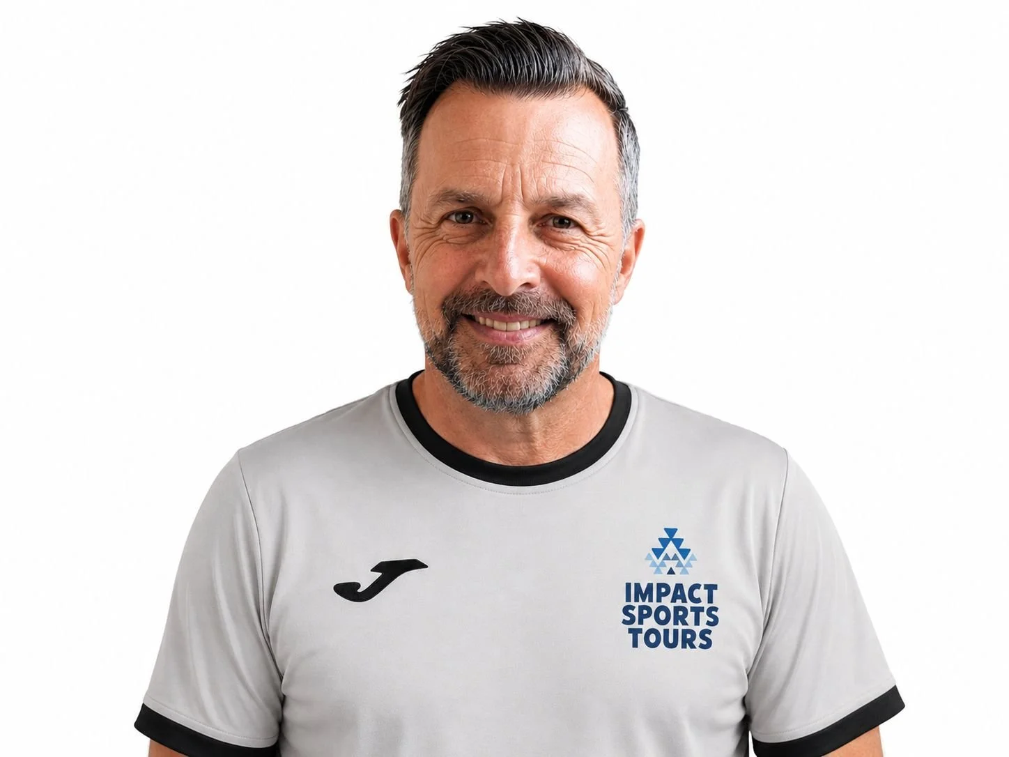 Smiling middle-aged man with gray hair and beard wearing a white sports shirt with black and blue accents, featuring the logos of Impact Sports Tours and Joma, standing against a plain white background.