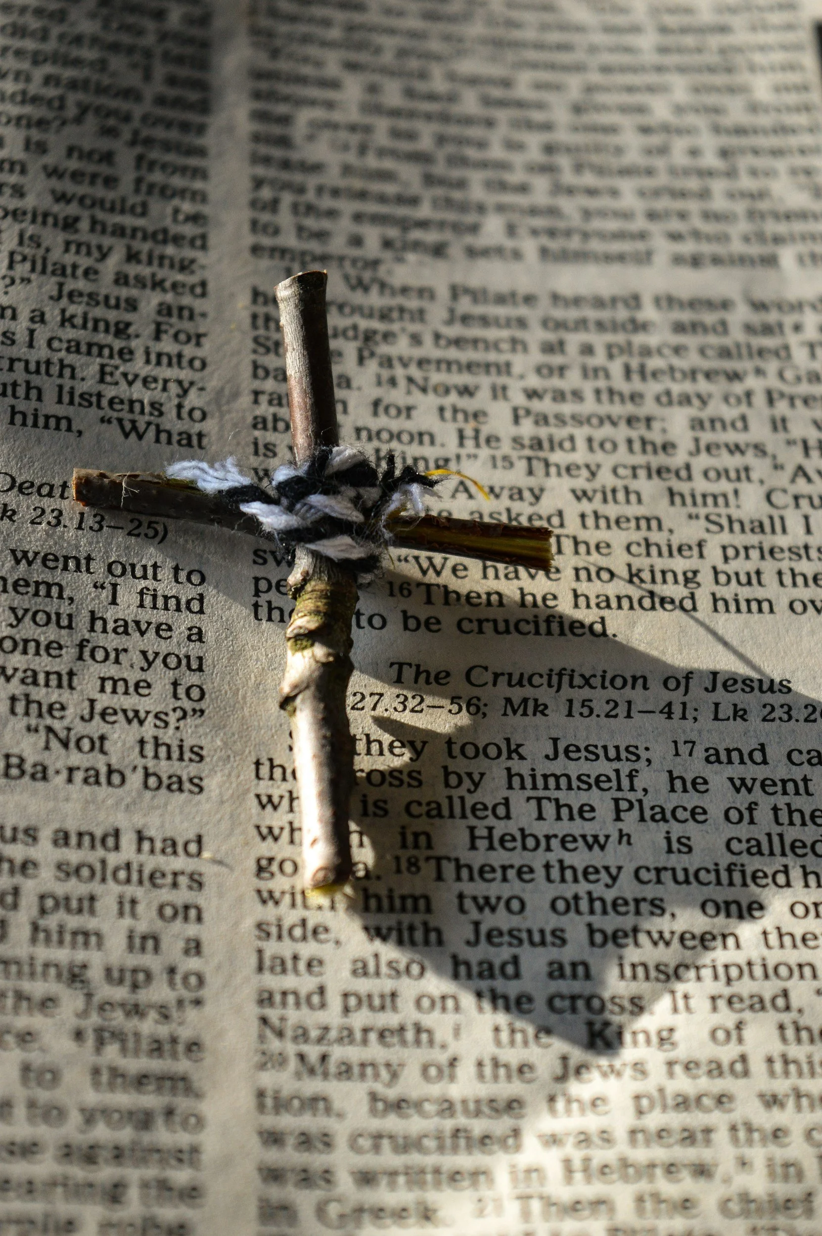 A small wooden cross wrapped with black and white cloth, placed on a newspaper with text.