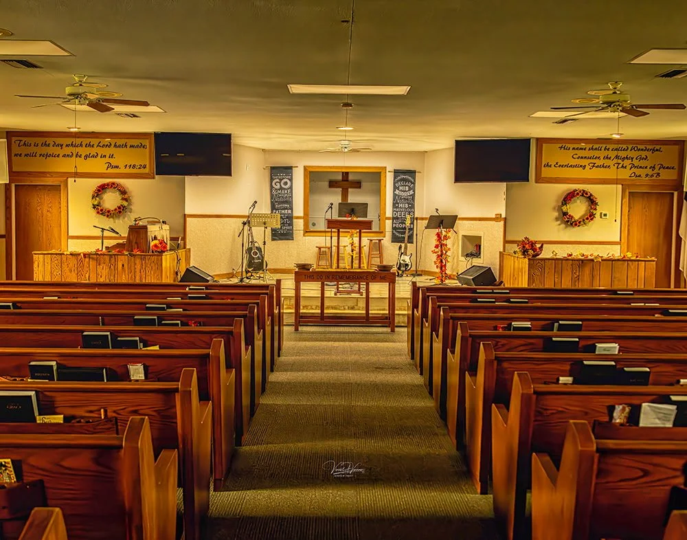 Empty church interior with wooden pews, altar, cross, including musical equipment, wreaths, and inspirational signs.