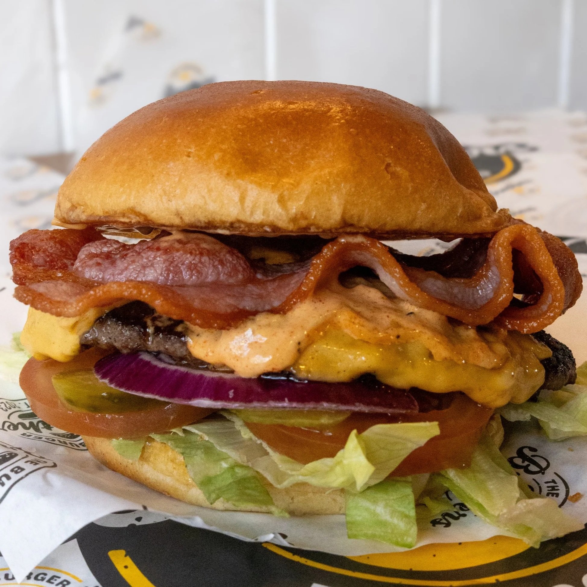 Close-up of a burger with bacon, cheese, lettuce, tomato, onions, and pickles in a bun.