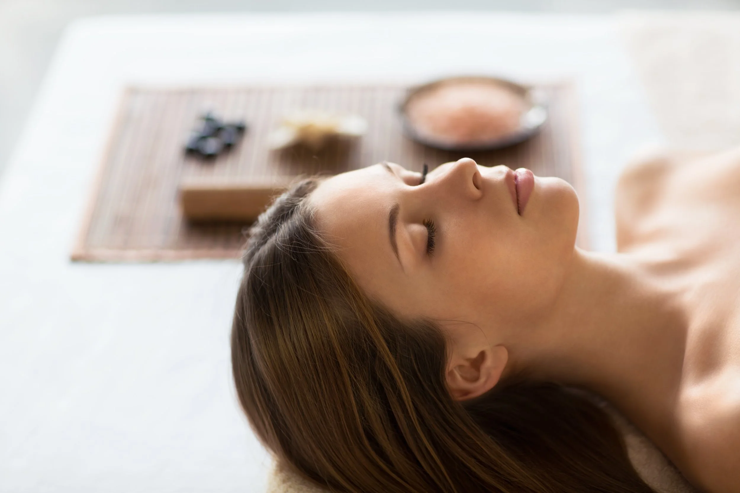 A woman with closed eyes and brown hair lying on her back on a massage table.