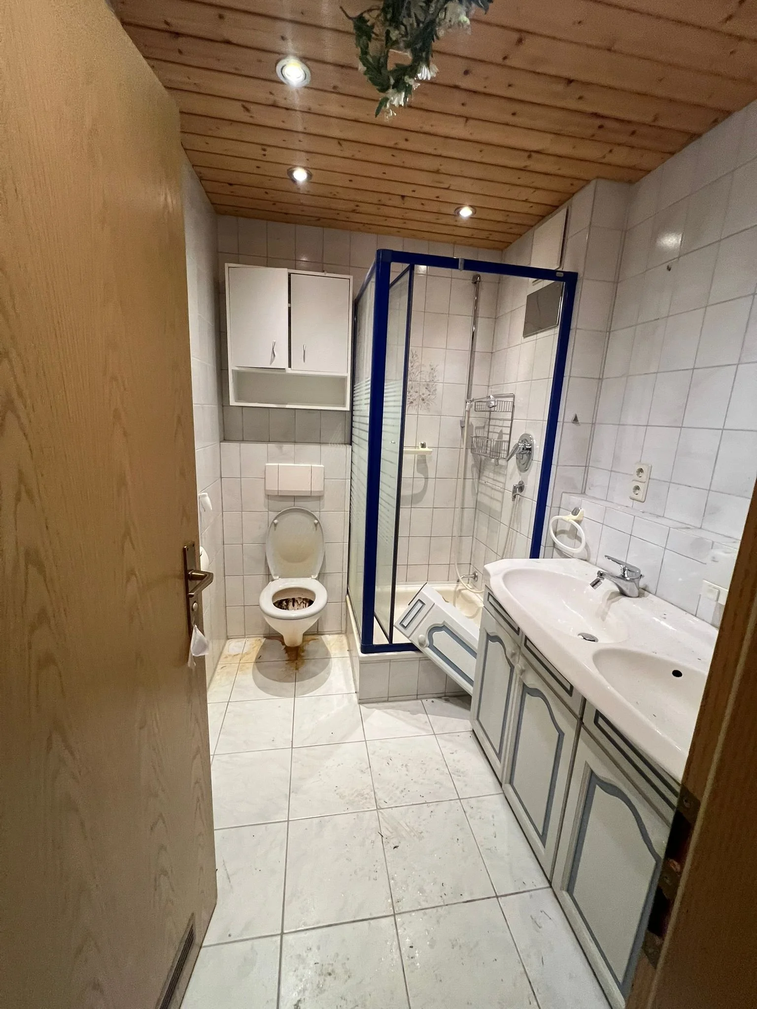 Ein unordentliches Badezimmer mit schmutzigen Fliesen, einem Toilette, einem Waschbecken und einer Dusche.