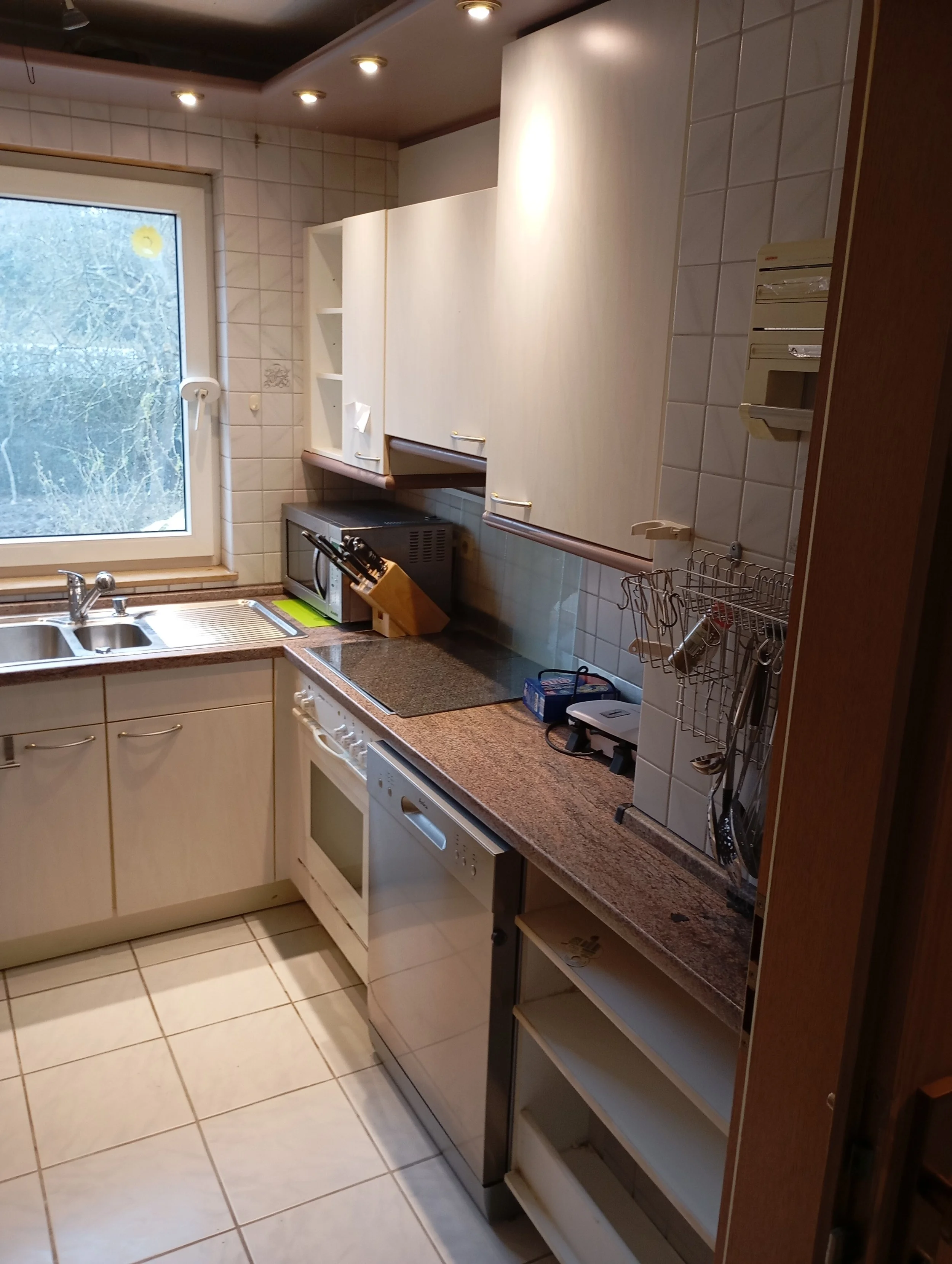 Kücheninsel mit Spüle, Herd, Mikrowelle, oberer und unterer Schrank, Fenster, Geschirrständer, elektrische Geräte, Küchengeräte, Geschirr und Küchenutensilien auf dem Arbeitsbereich.