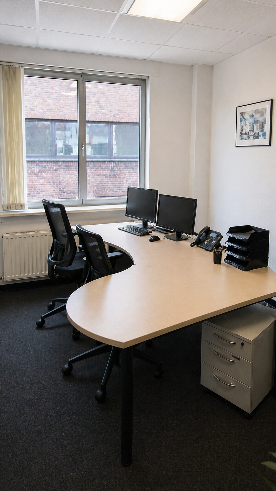 Büro mit zwei Computermonitoren, Telefon, Schreibtisch mit Stühlen, Ablagefächer, Fenster und einem Bild an der Wand.