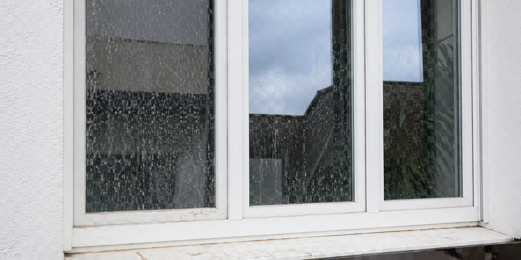 Fenster mit Regentropfen, Blick auf den Himmel und das Dach eines Hauses.