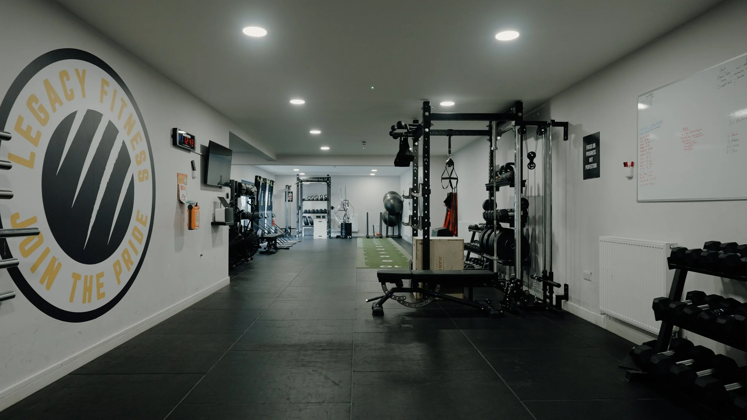 Empty gym with workout equipment and a mural on the wall that reads "Legacy Fitness - Move in the Pace".