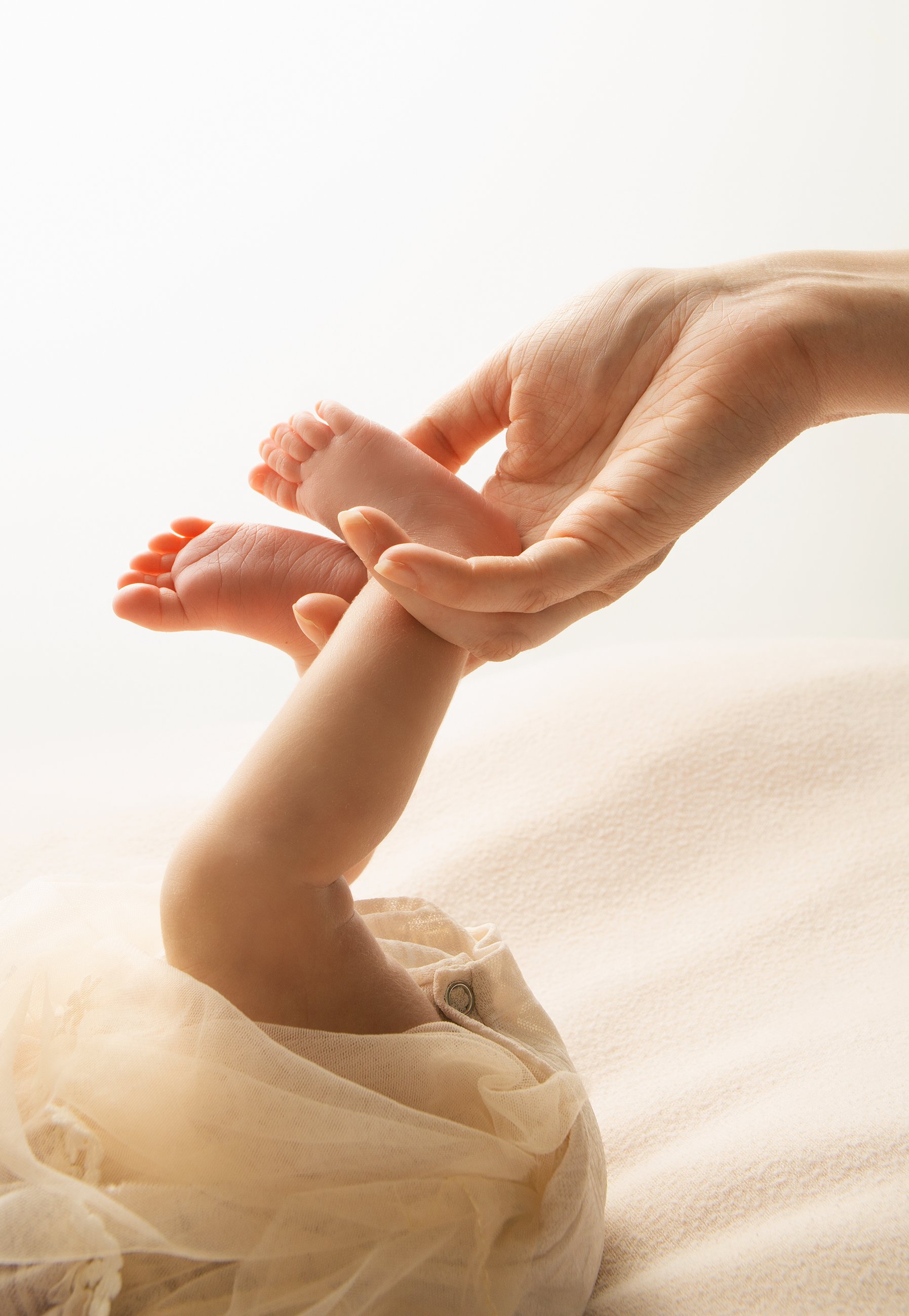 A hand holding a tiny baby foot, with the baby's leg resting on a soft, light-colored surface.