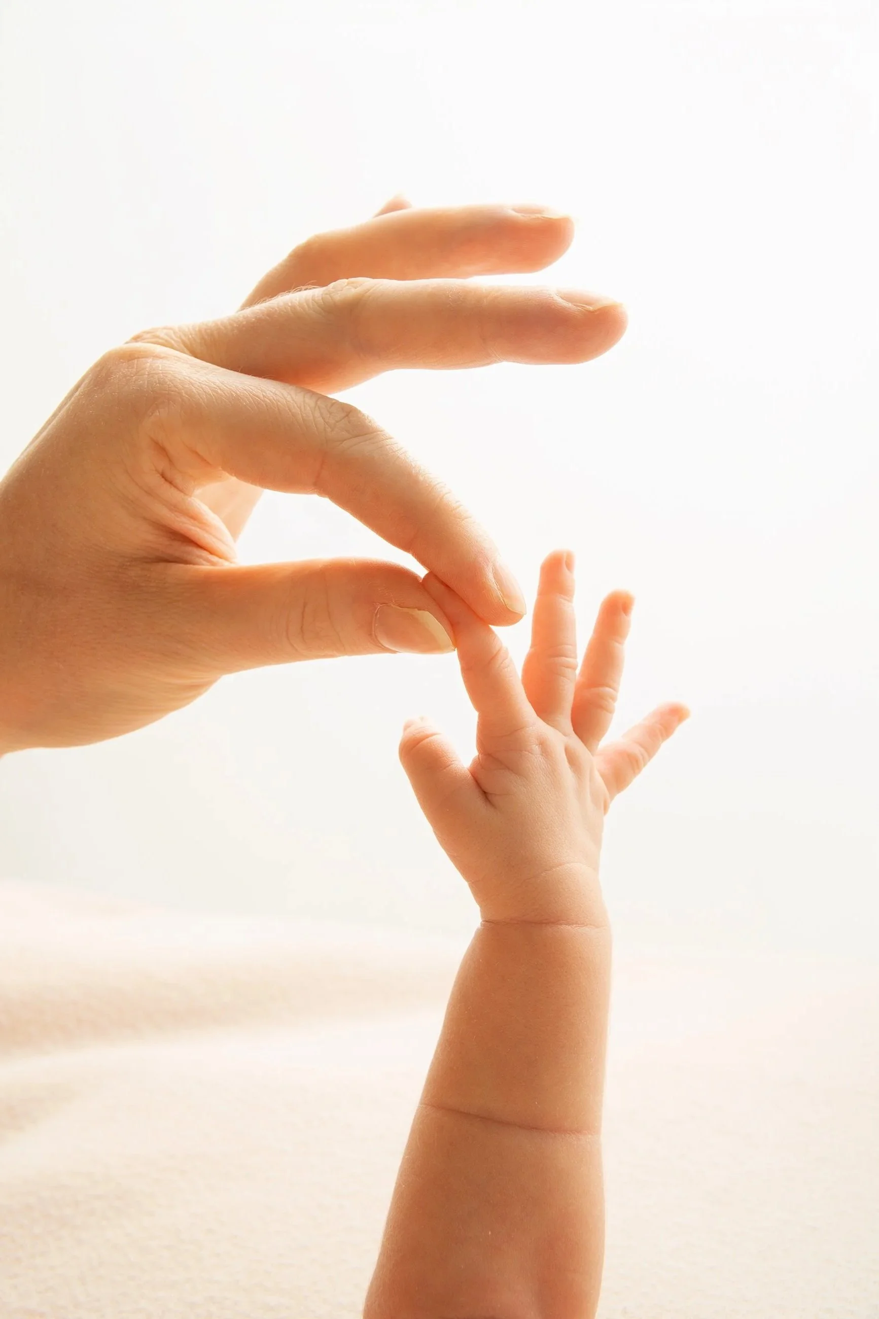 A hand with neatly trimmed nails holds a small child's hand against a bright, white background.