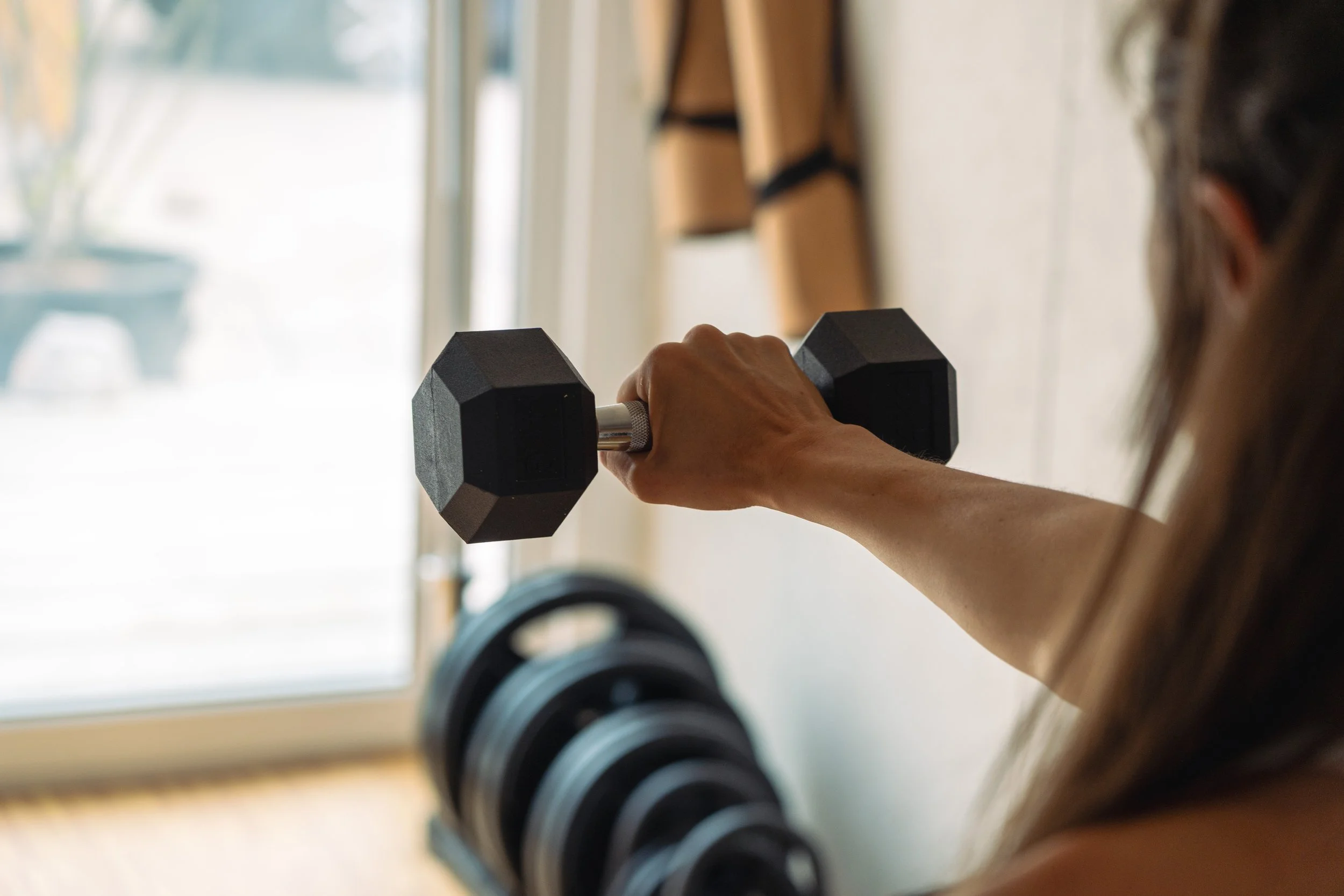 A person holding a black dumbbell while doing exercises with a row of other dumbbells visible on the floor nearby.