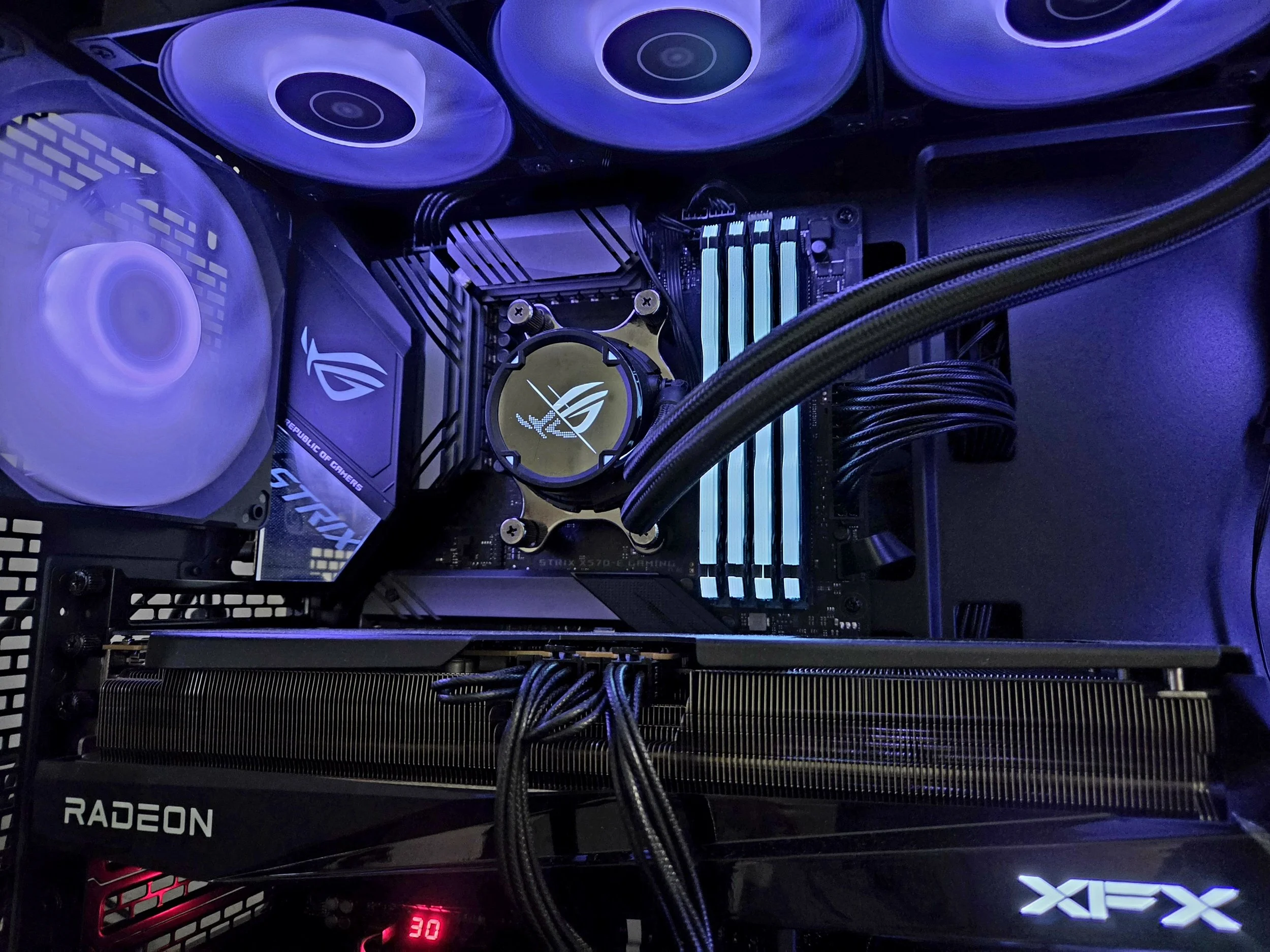 Inside a gaming PC with illuminated components, showing cooling fans, a motherboard, a water cooler, RAM sticks, a Radeon graphics card, and various cables.