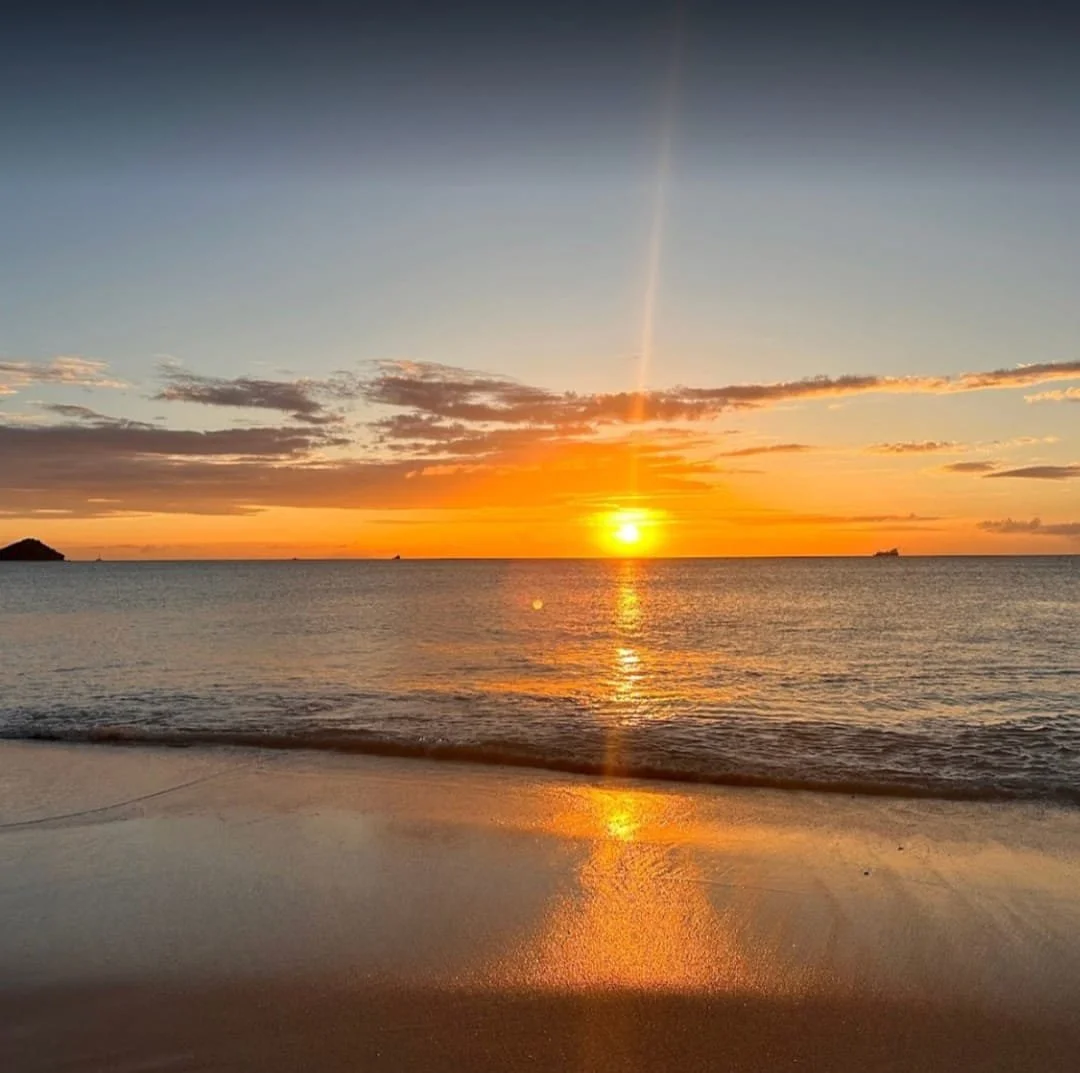 Sunset over the ocean with reflection on the wet sandy beach and a few clouds in the sky.