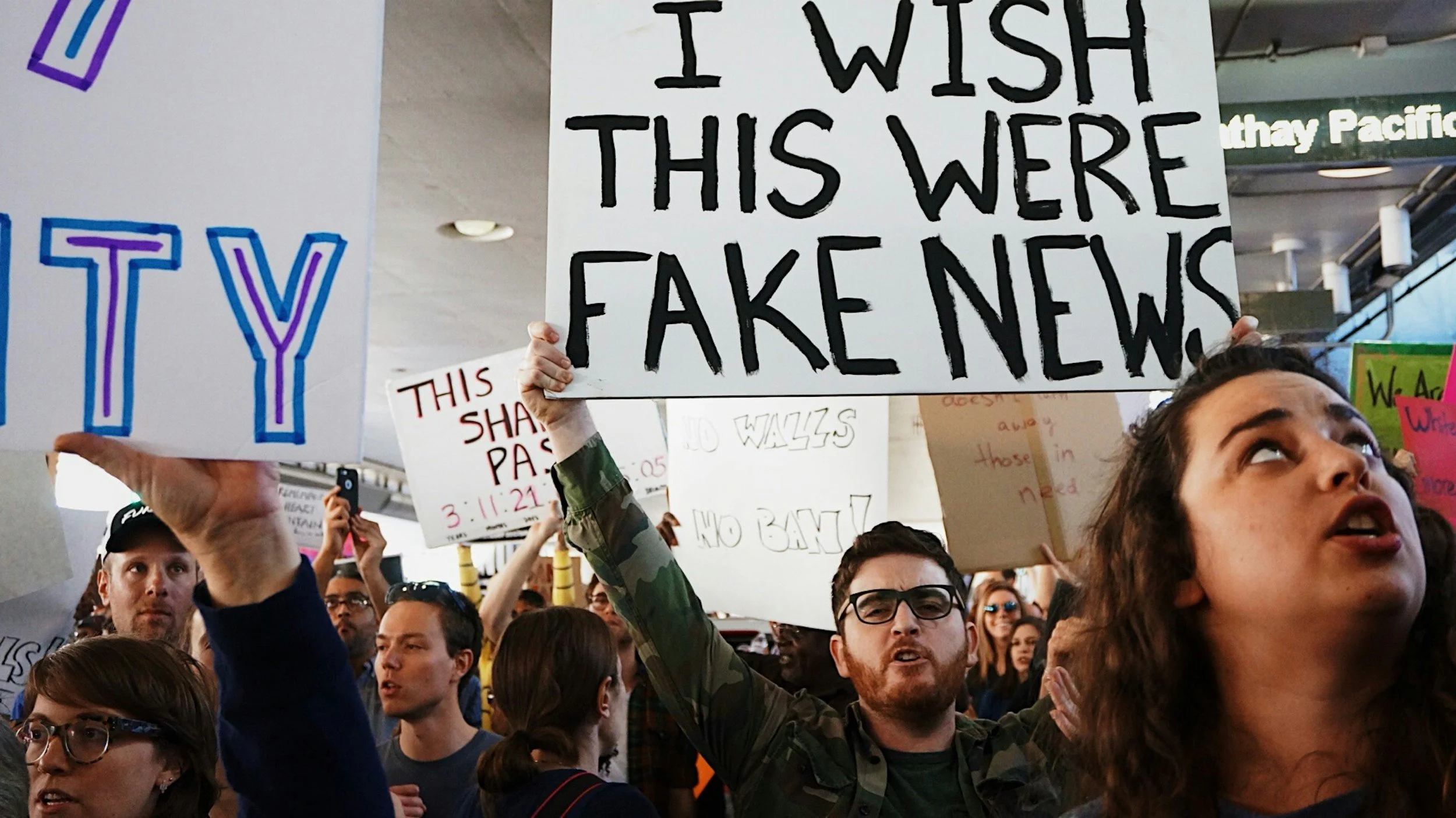 Un groupe de manifestants tiennent des pancartes avec des messages contre les fausses informations, dont une qui dit : « Je souhaite que ceci était des fausses nouvelles ».
