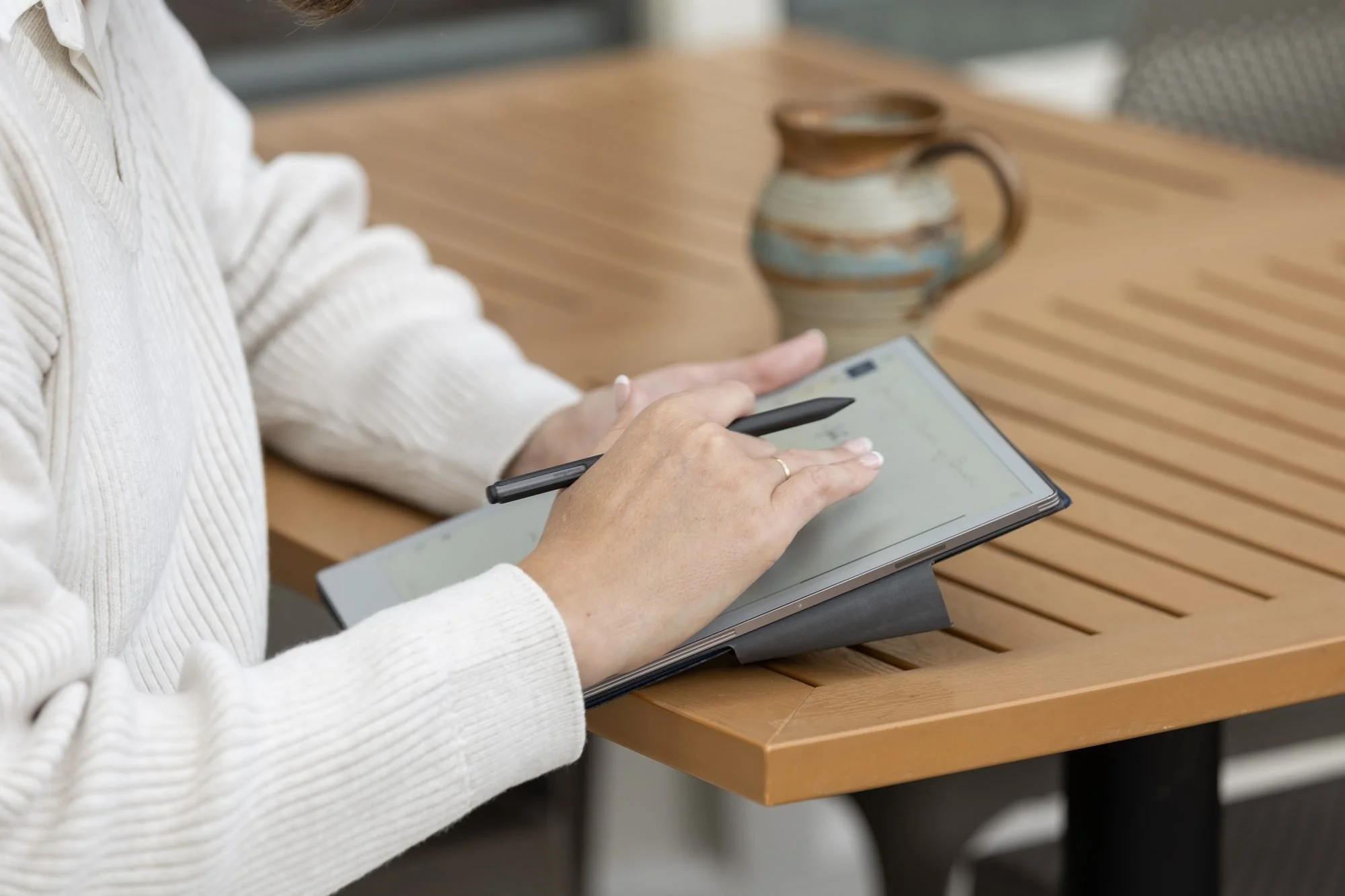 Hands writing on a tablet with a stylus beside a ceramic mug on a wooden table
