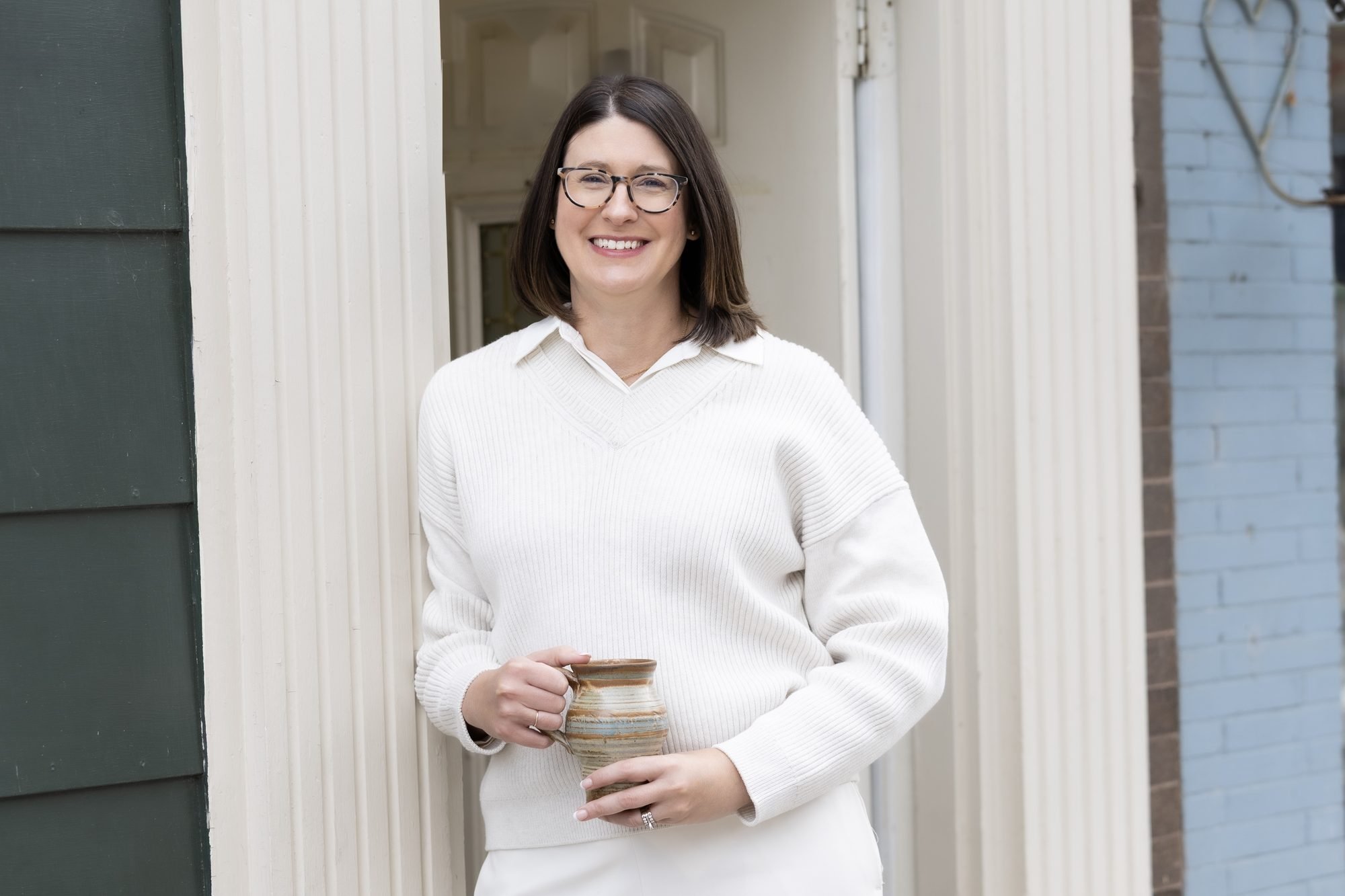 Jill Decker, LPCC, smiling in an open doorway holding a ceramic mug