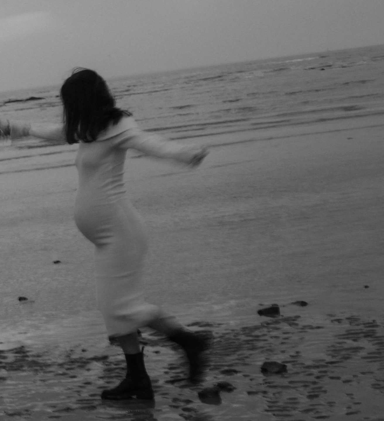 Une femme marche sur la plage avec la mer en arrière-plan, en noir et blanc.