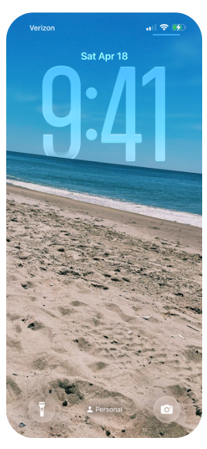 OLED iPhone lock screen showing the time 9:41 on Saturday, April 18, with a background of a sandy beach and ocean under a partly cloudy sky.