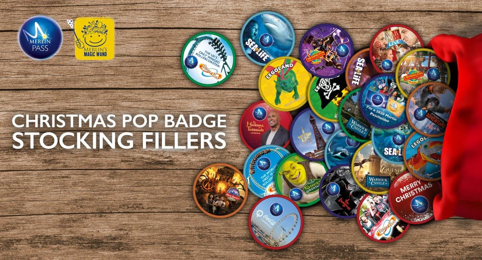A collection of Christmas-themed Merlin Pass badge stickers on a wooden surface, spilling out of a red stocking, with text reading 'Christmas Pop Badge Stocking Fillers'.