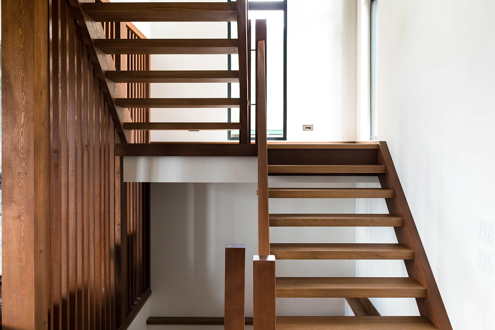 Modern open-riser wooden staircase with dark wood railings and white walls