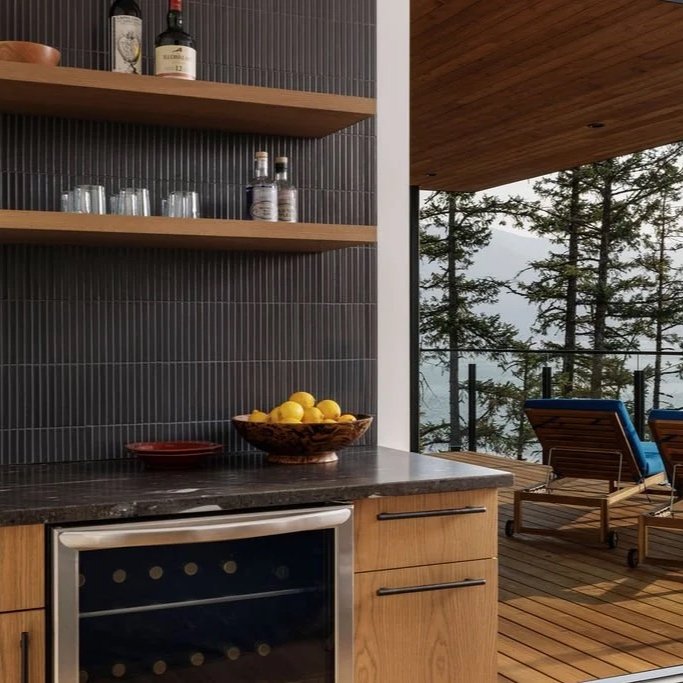 View from a kitchen to outdoor balcony with two lounge chairs, overlooking trees and misty mountains.