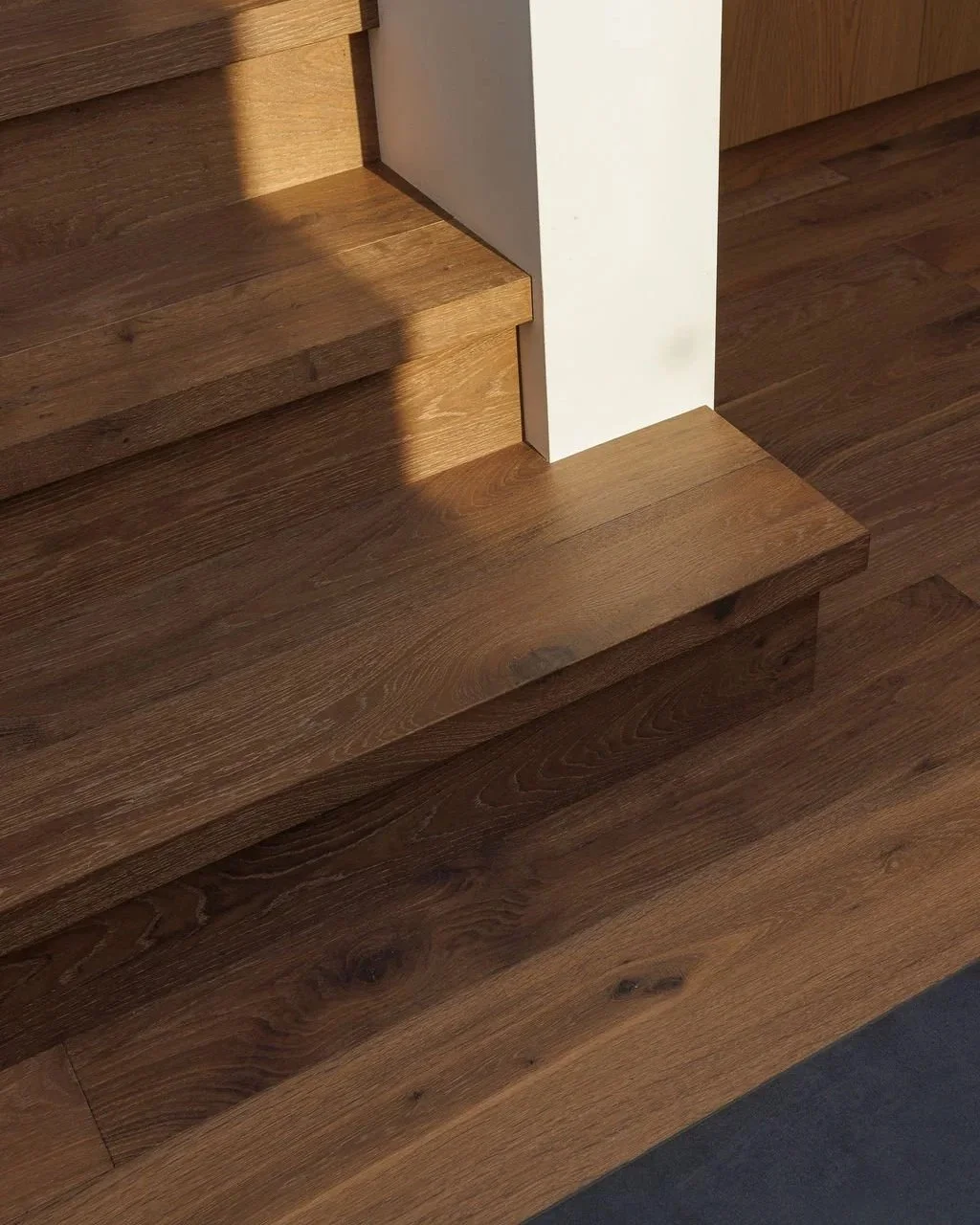 Close-up of a wooden staircase with a white wall corner and hardwood flooring.