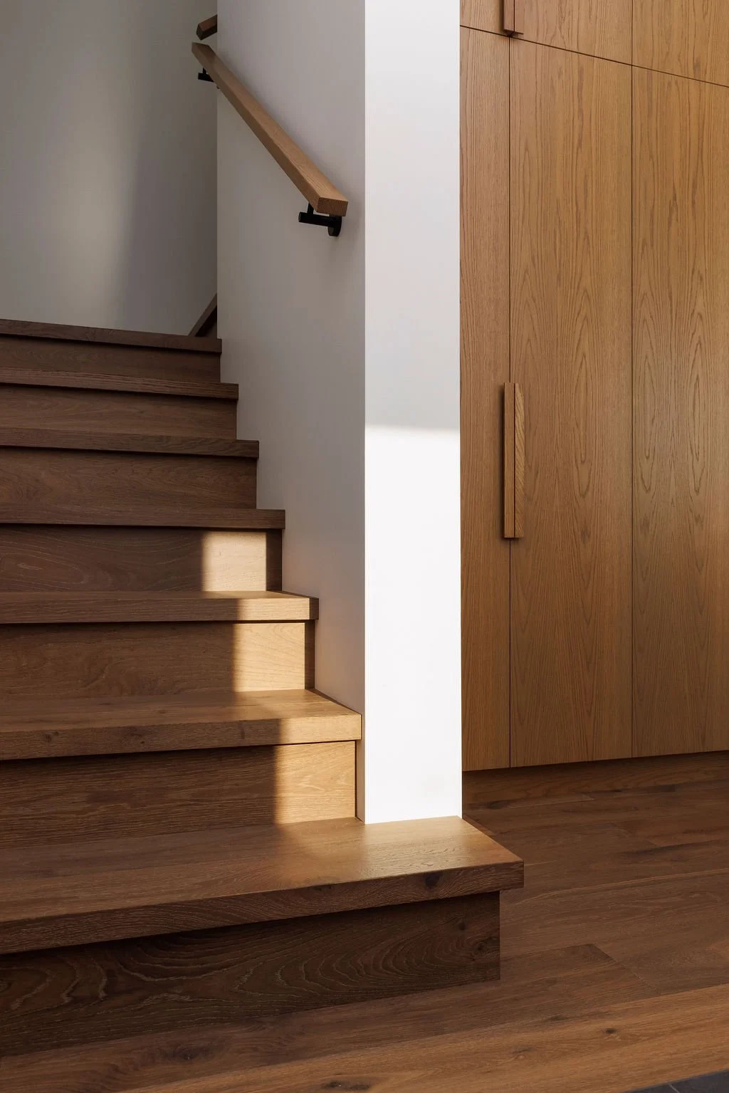 Interior view of a modern wooden staircase with matching wooden cabinetry, illuminated by natural light.
