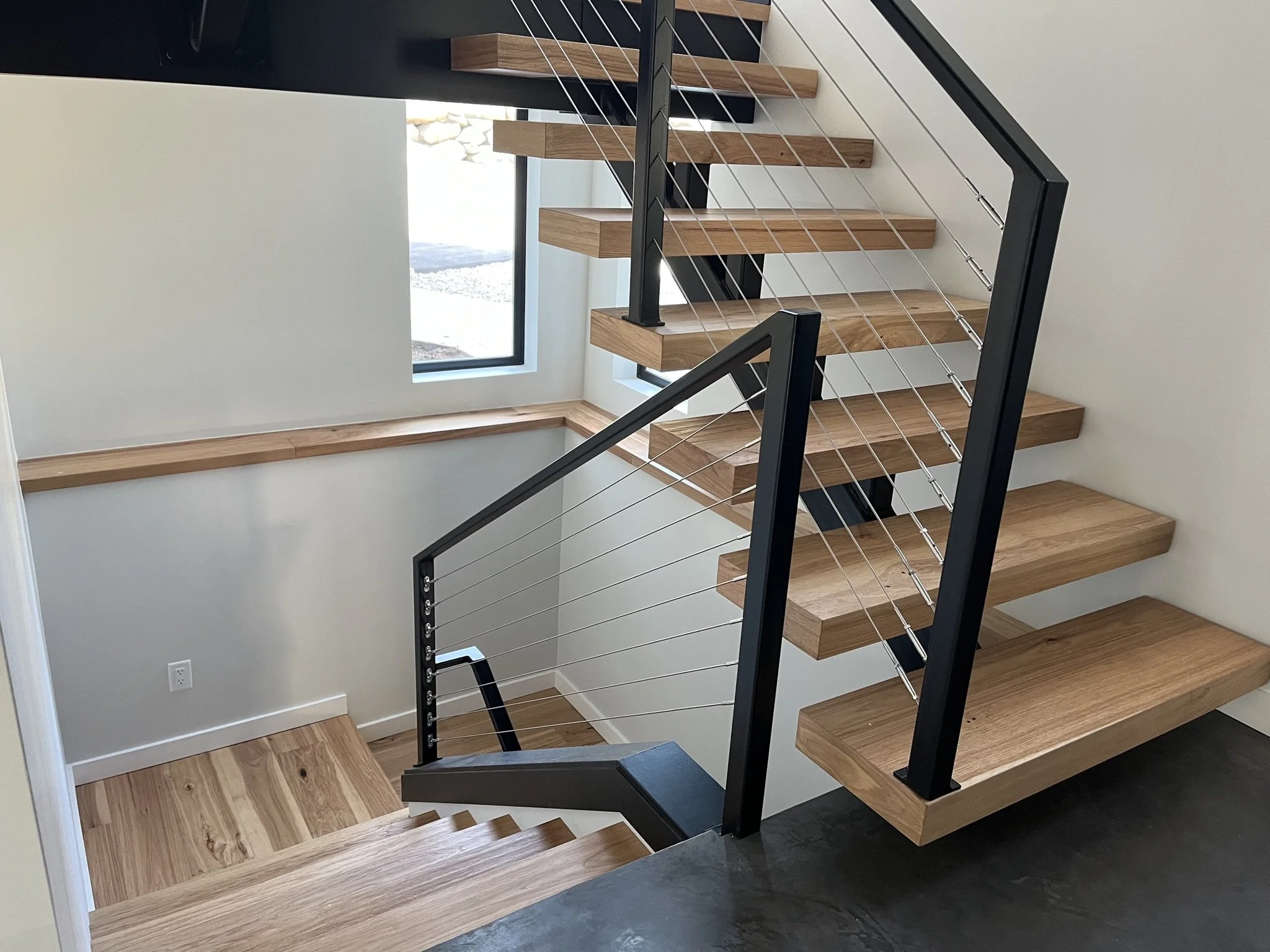 Modern multi-level floating wood staircase with black steel frames and cable railings
