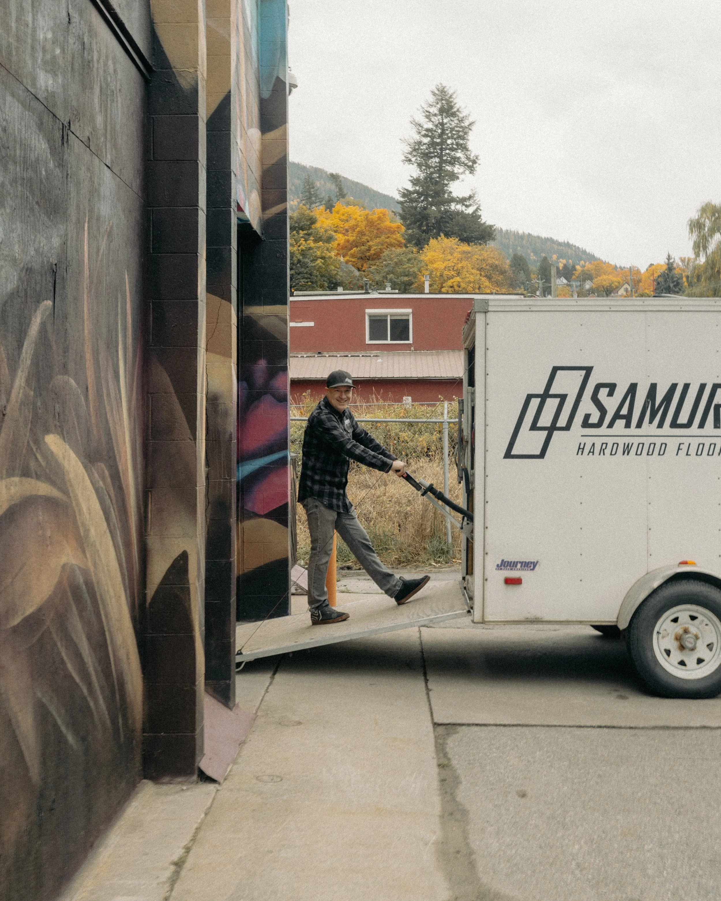 Man moving a hardwood flooring trailer through an alley with autumn trees and mountains in the background