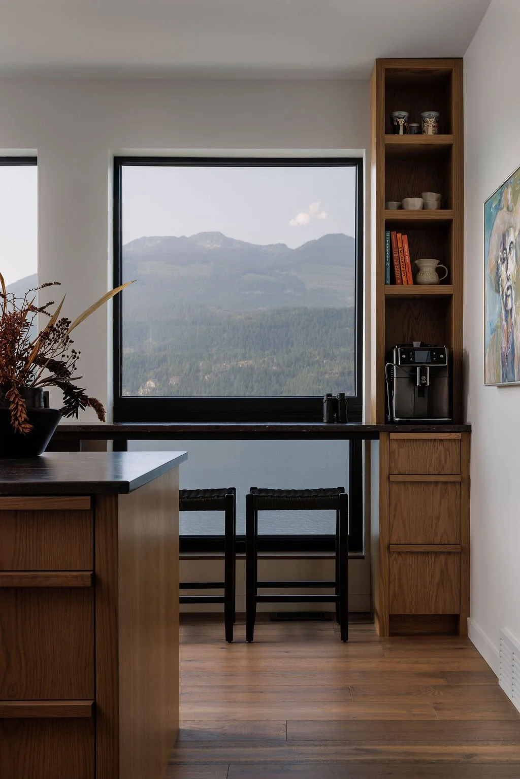 Modern kitchen with wood cabinetry, built-in coffee maker, bar stools, and mountain views through a large window