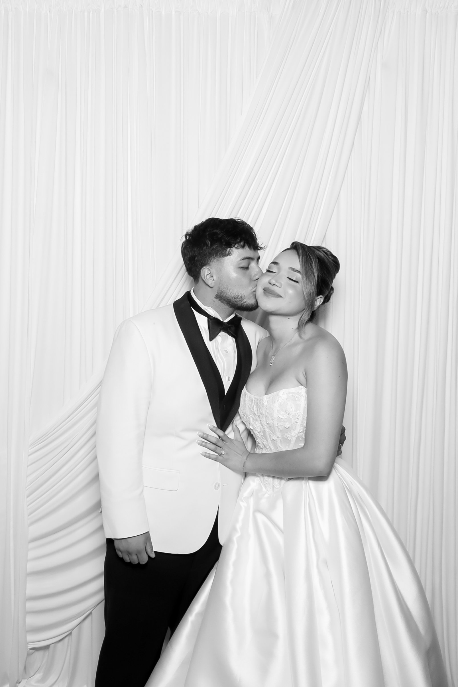 Black and white wedding photo booth portrait of a couple posing in front of an elegant white drape backdrop by Bella Photobooth in Atlanta, Georgia