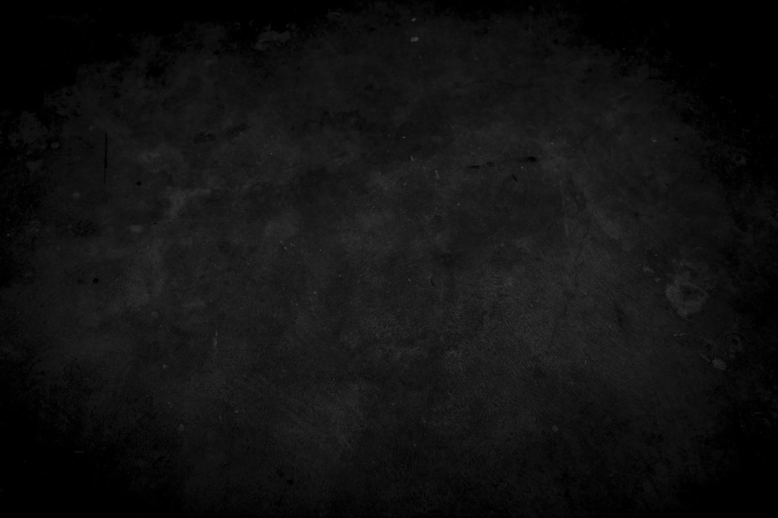 A dark, black textured surface with some debris and slight scratches visible.
